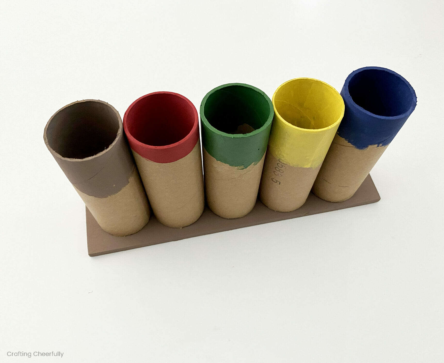 Piece of wood with five cardboard tubes lined up on it..