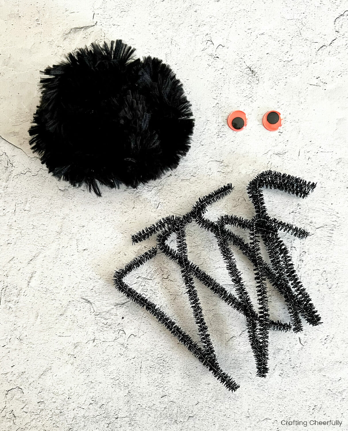 Large pipe cleaner balled up, two orange googley eyes and eight thin pipe cleaners with one of their ends bent.