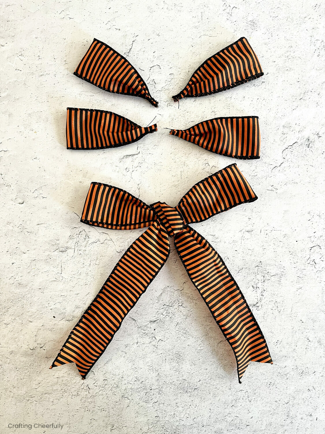 Black and orange striped ribbon bow with four ribbon loops laying near it.