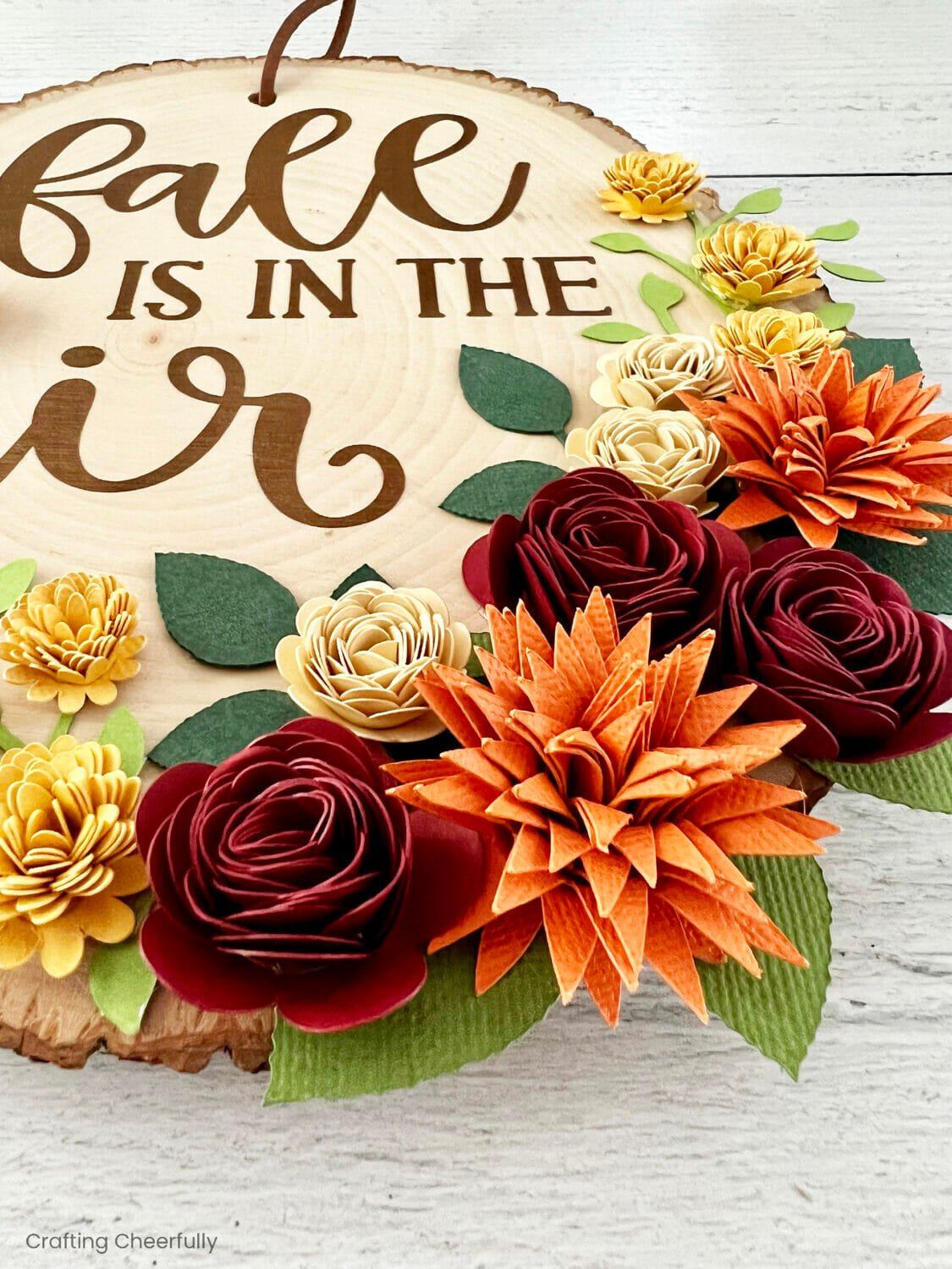 Beautiful paper flowers decorate the bottom of a wood slice sign.