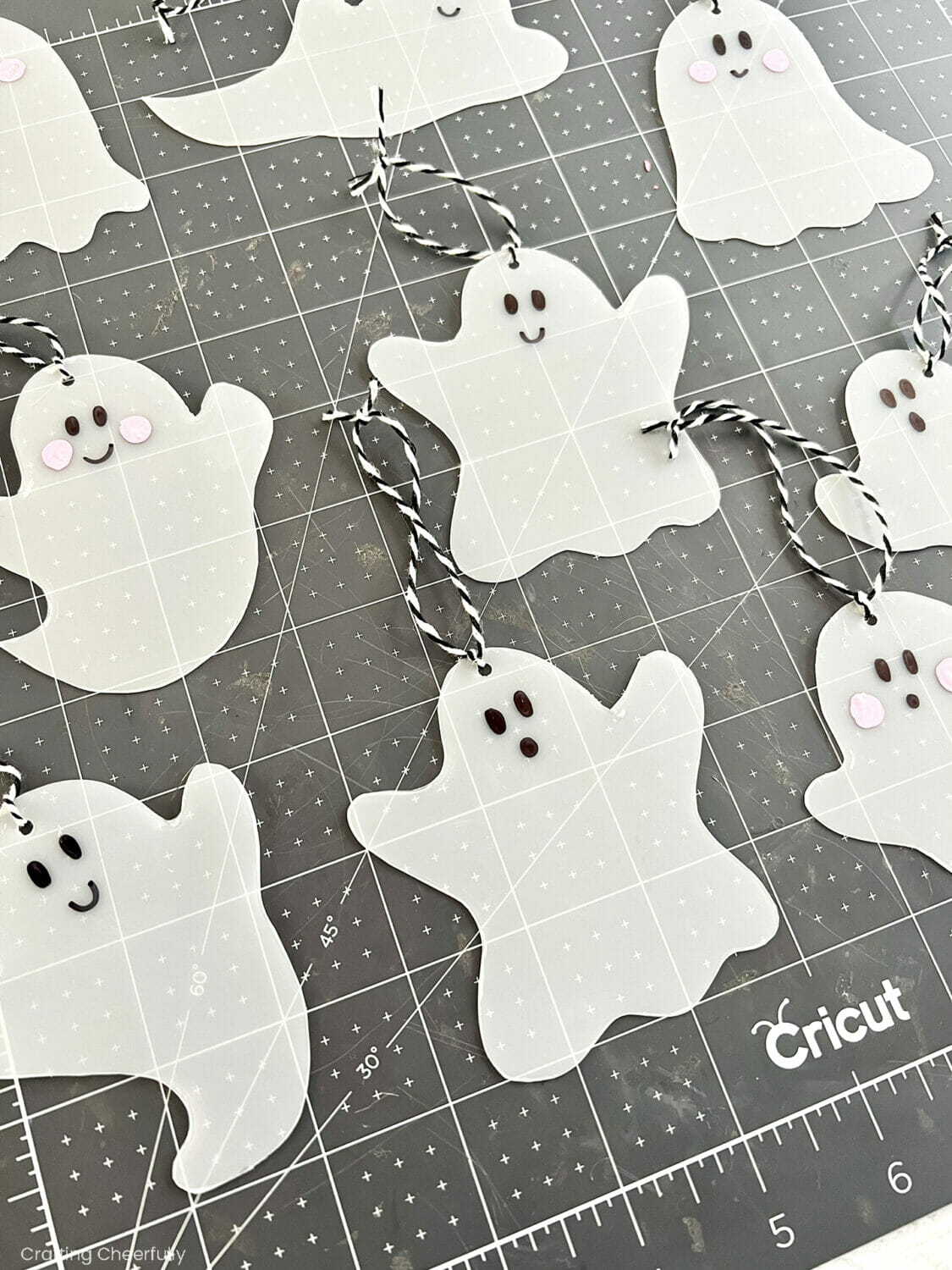 Ghost ornaments lay on a black cutting mat with faces and hanging loops.
