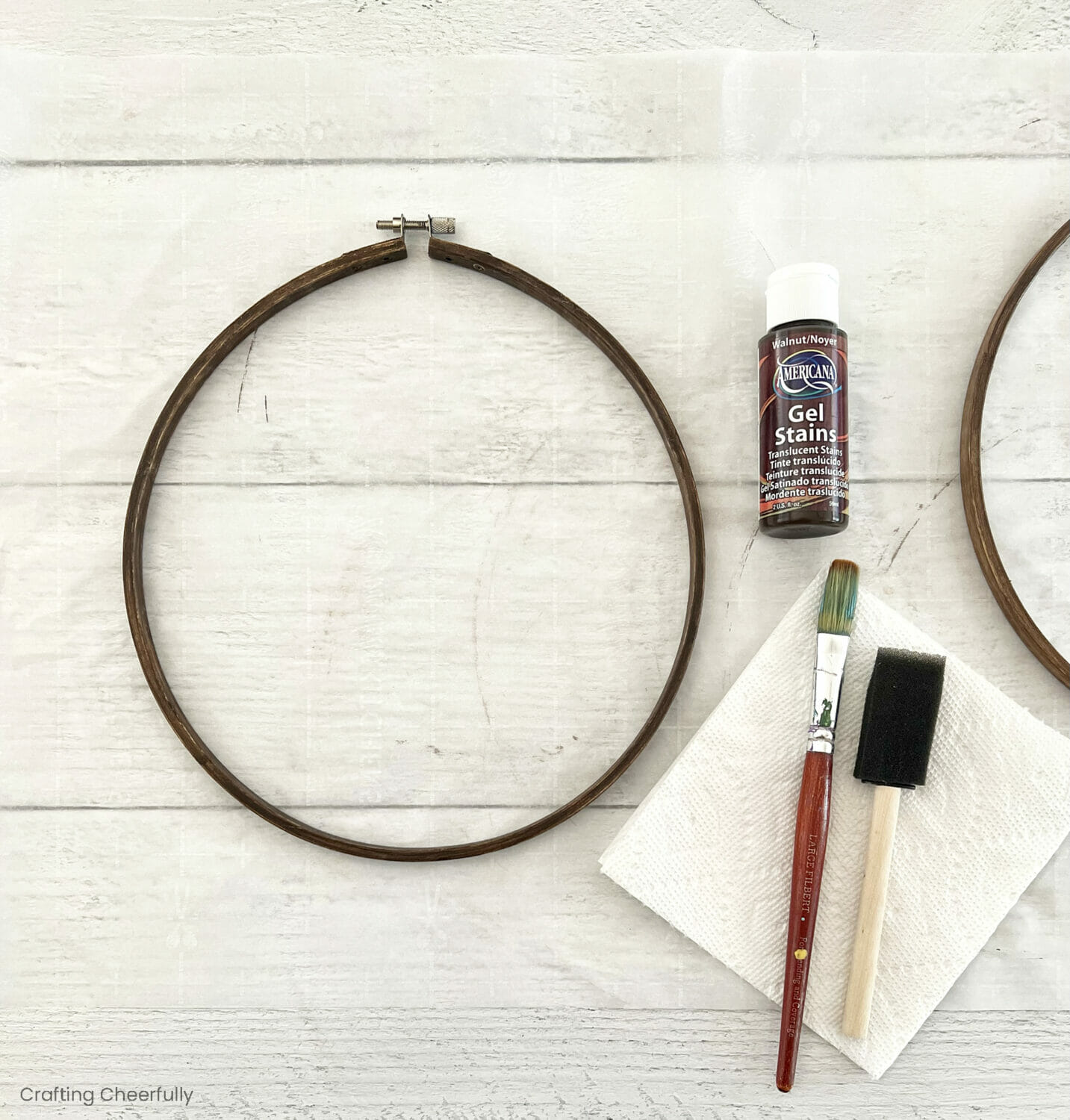 A stained hoop lays next to a bottle of gel stain, a paint brush and a foam brush.