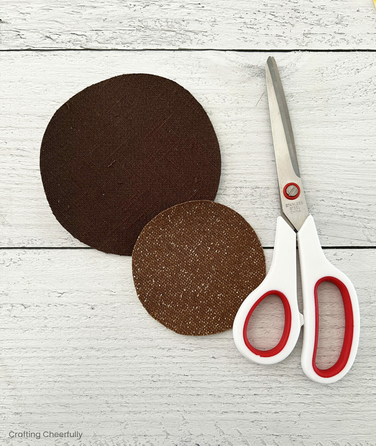 Two brown circles of fabric lay next to a pair of scissors.