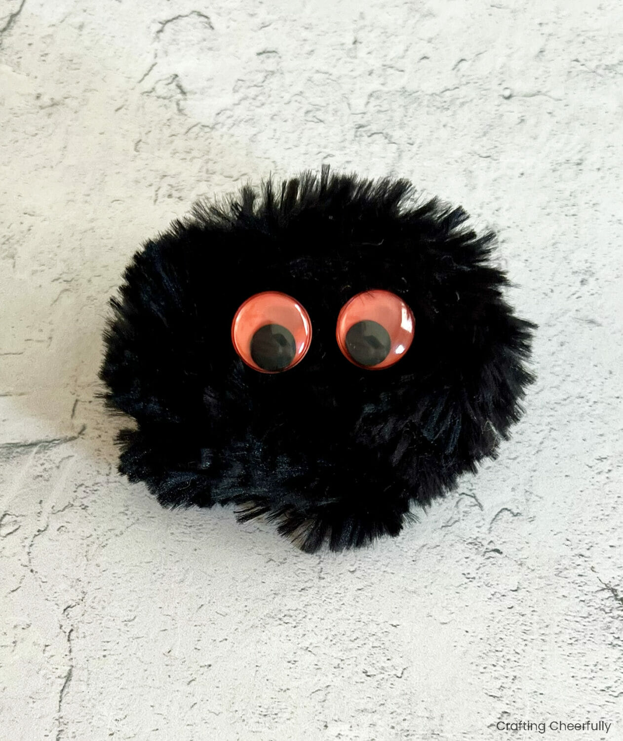 Two orange googley eyes are glued to the top of the black fluffy pipe cleaner ball.