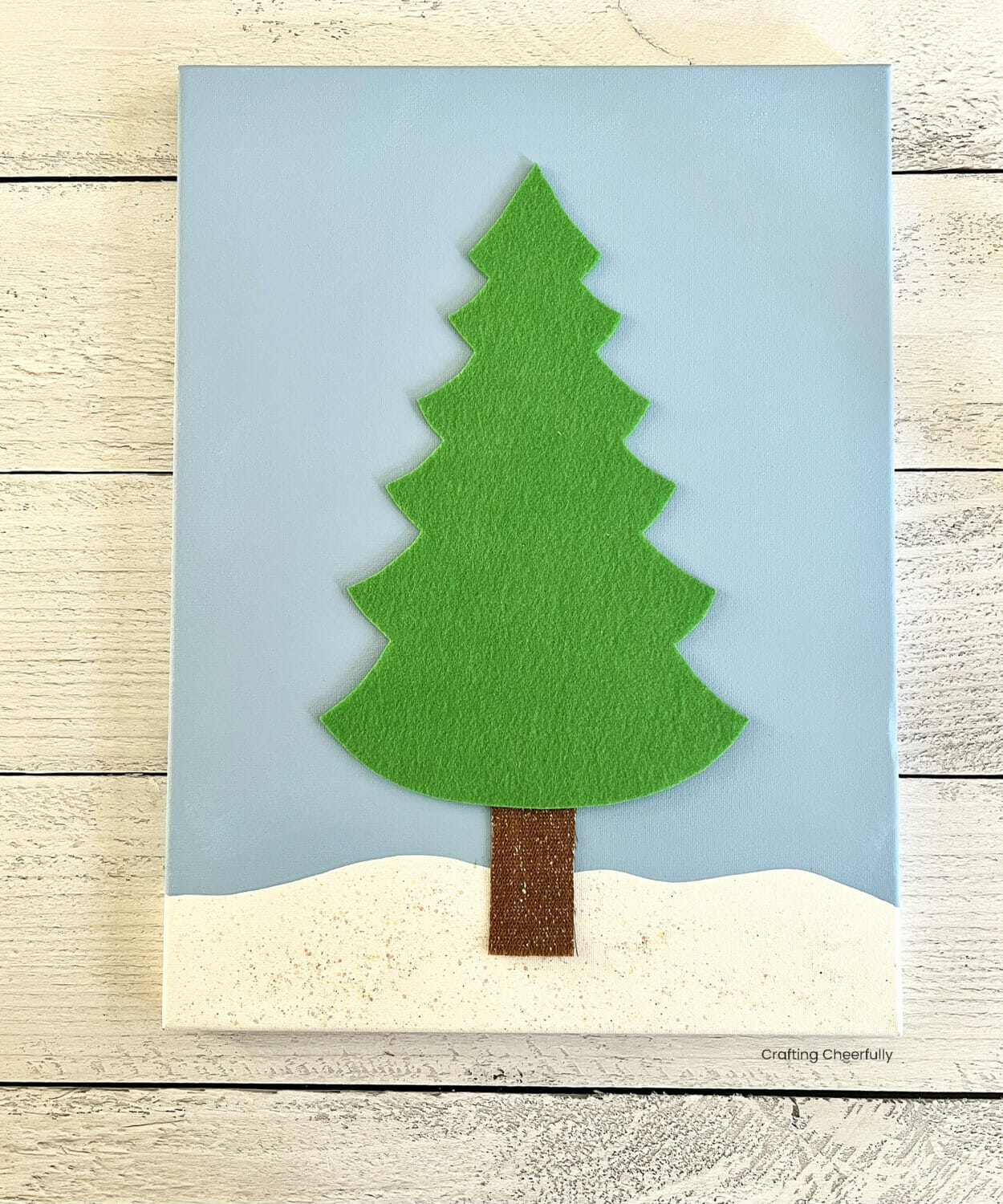 A green felt tree and brown fabric trunk are laid on the canvas.