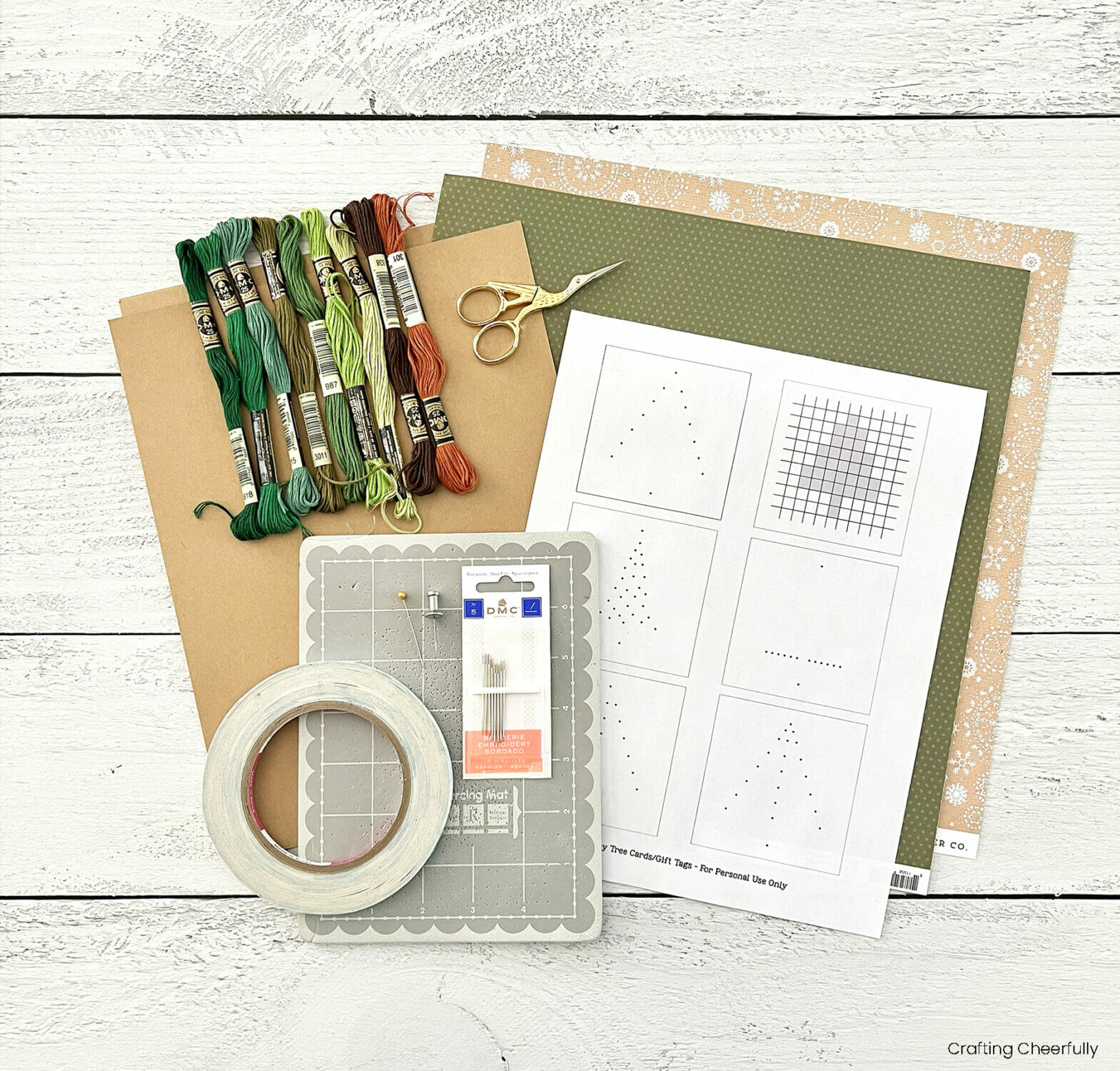 Cardstock, stitching pattern, double-sided tape, embroidery floss, scissors and piercing mat lay on a wooden table.