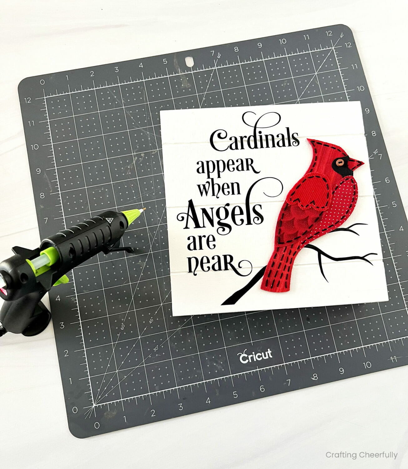 A red felt and fabric appliqué bird is glued to the wooden sign so it appears to be sitting on a black branch.