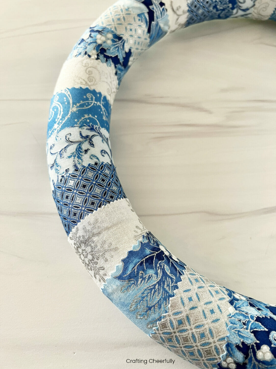 Foam wreath form wrapped with blue, silver and white fabric strips.