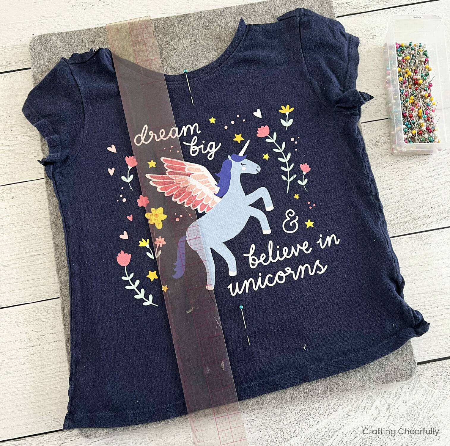 A ruler measures around the design on the t-shirt and is marked with pins.