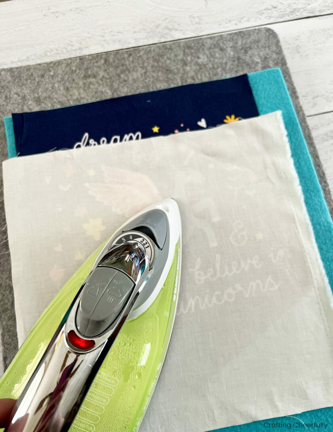 The t-shirt is ironed to the teal felt using a pressing cloth.