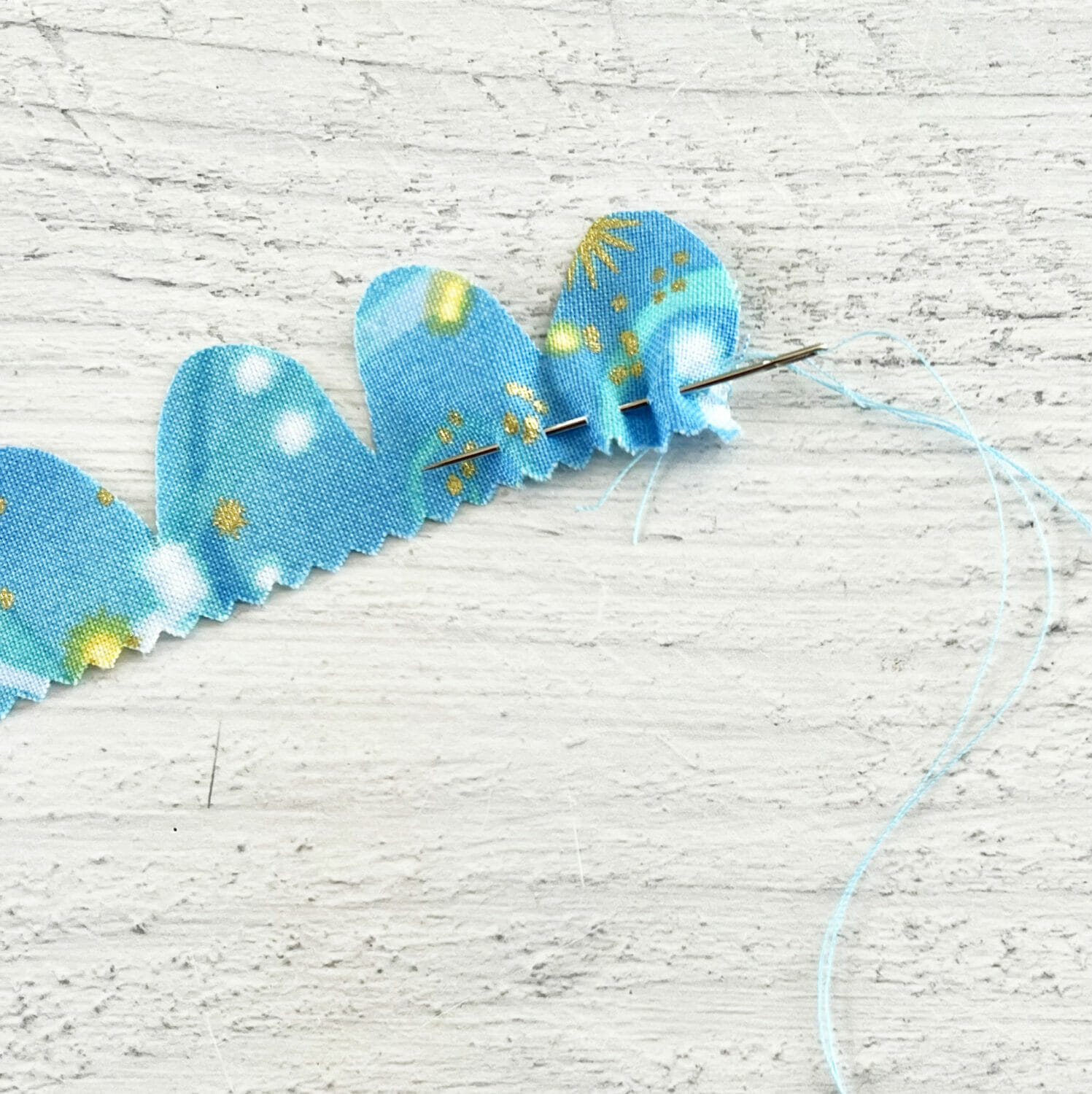A needle and thread goes through the bottom edge of the scalloped fabric strip.