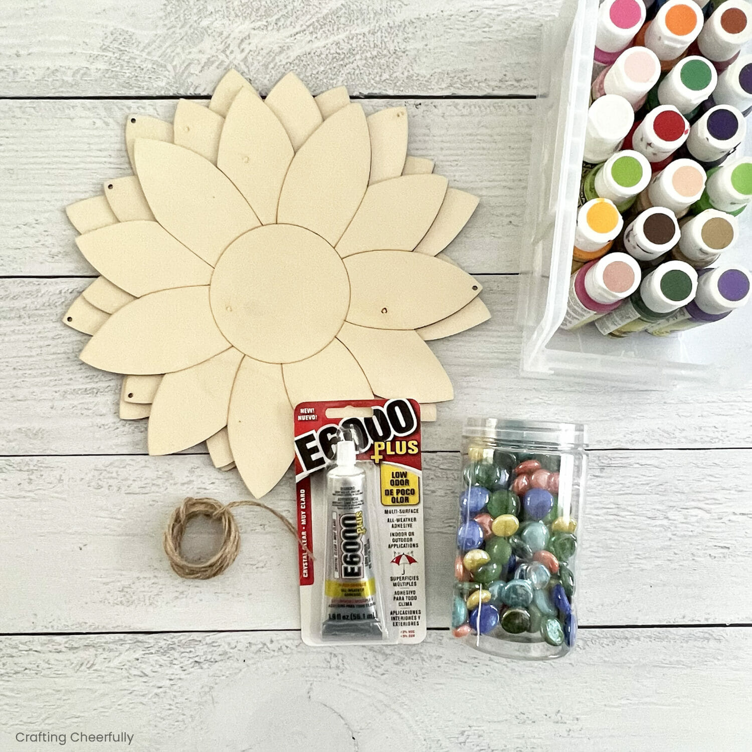Three wooden flowers lay next to outdoor paint, twine, E6000 glue and glass beads.