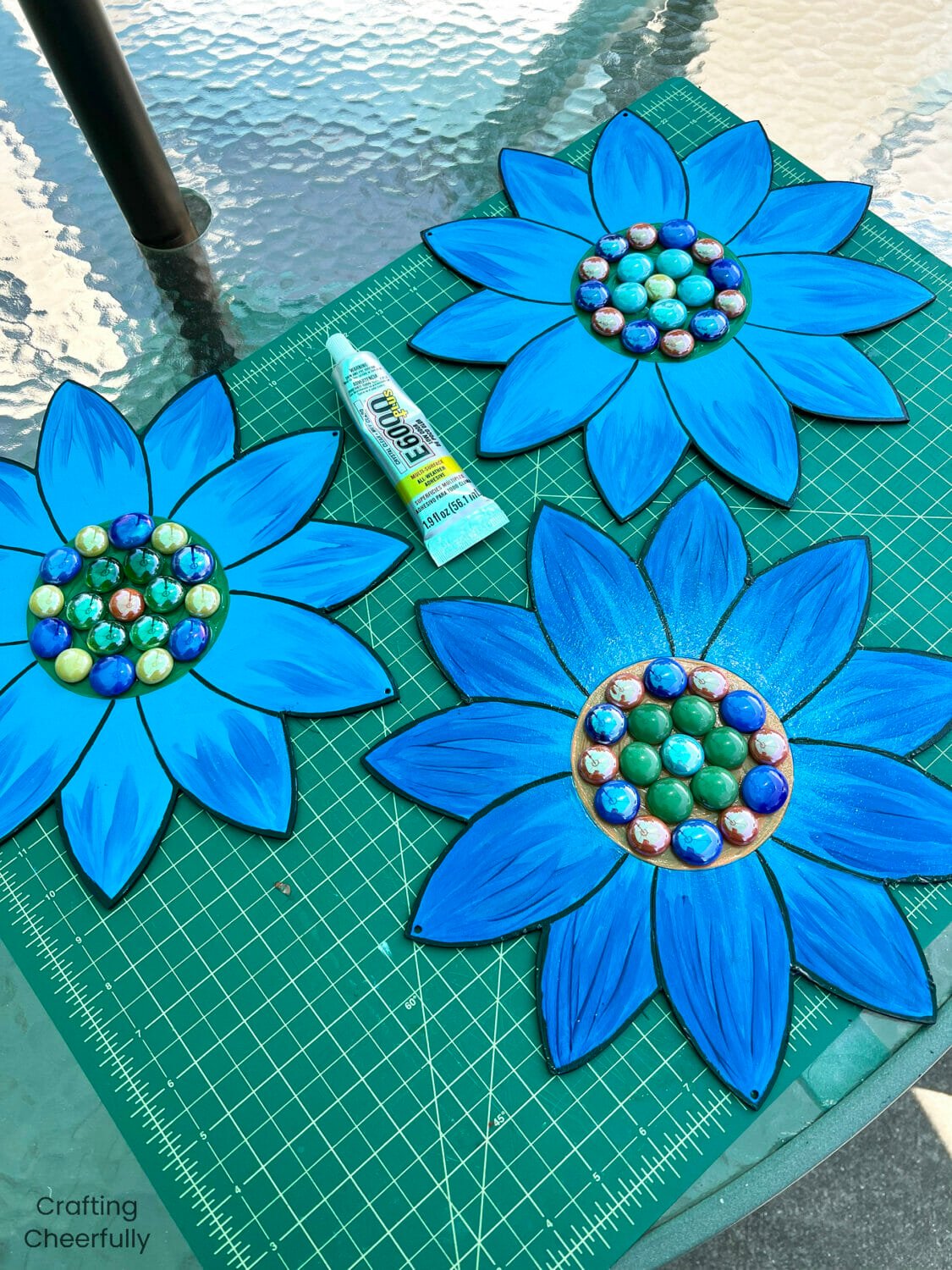 Three wood flowers painted blue have gemstones attached to the center.