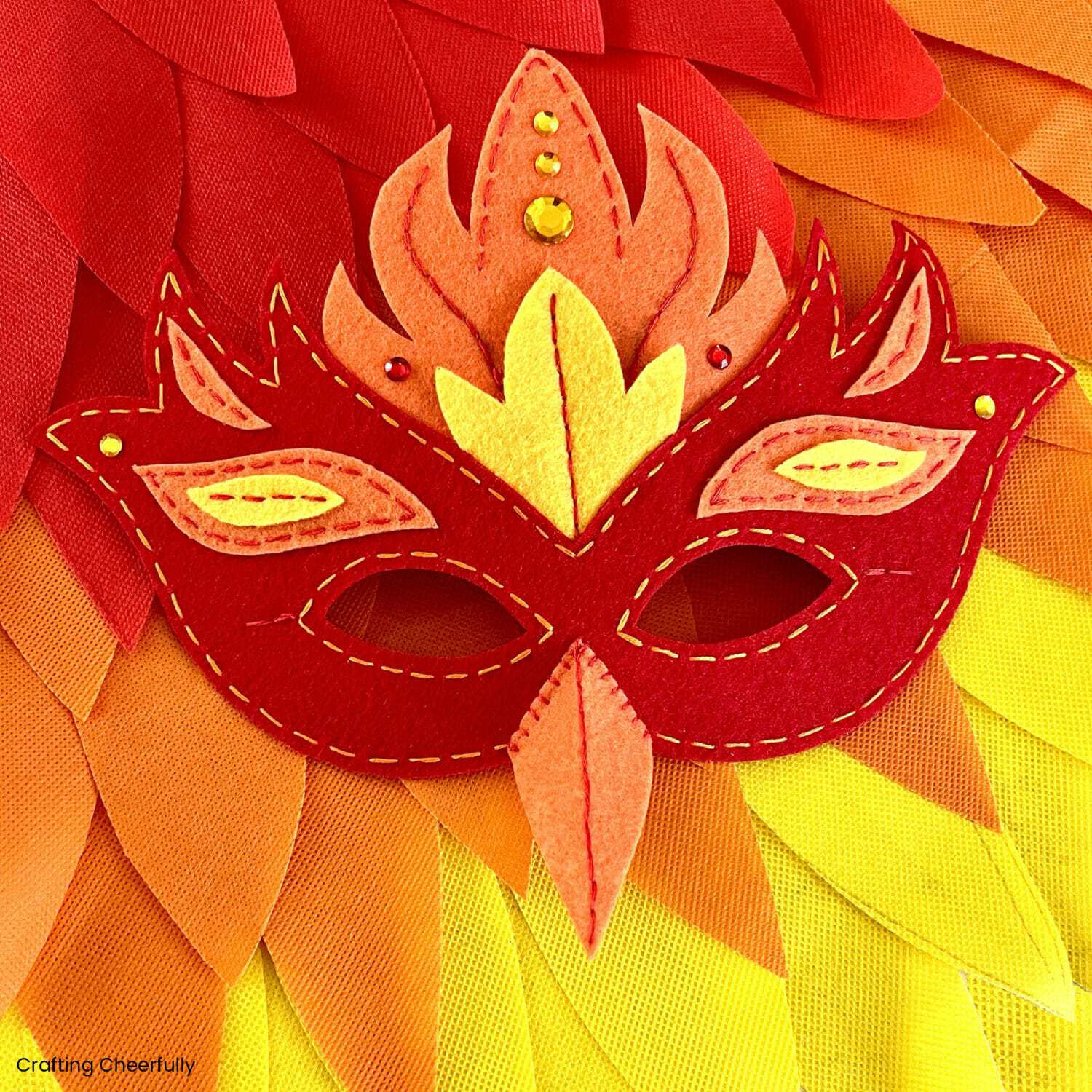 Felt phoenix mask lays on on top of the phoenix costume made from red, orange and yellow feathers.