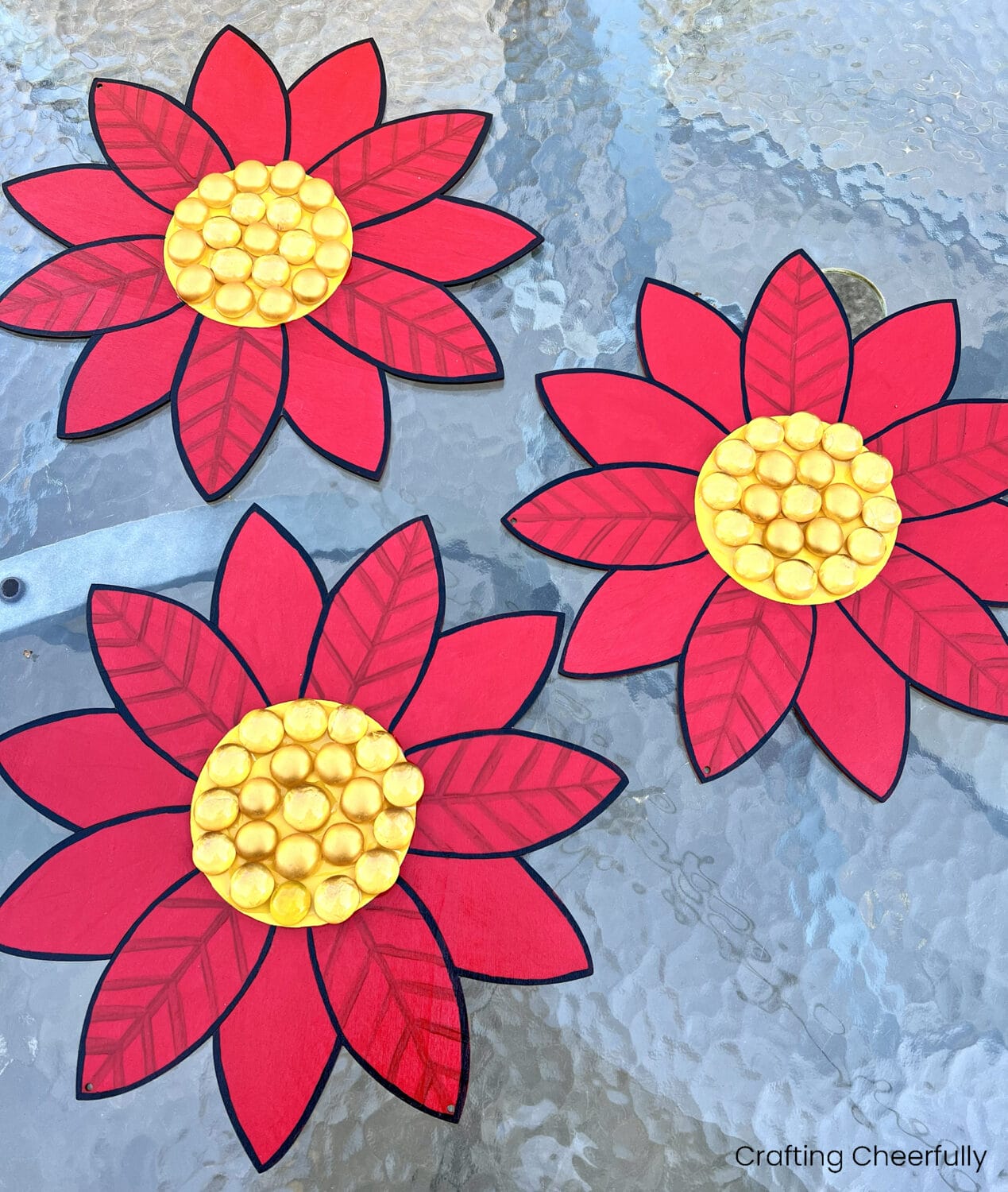 Wooden poinsettias with gold gemstones added to the center of the flowers.