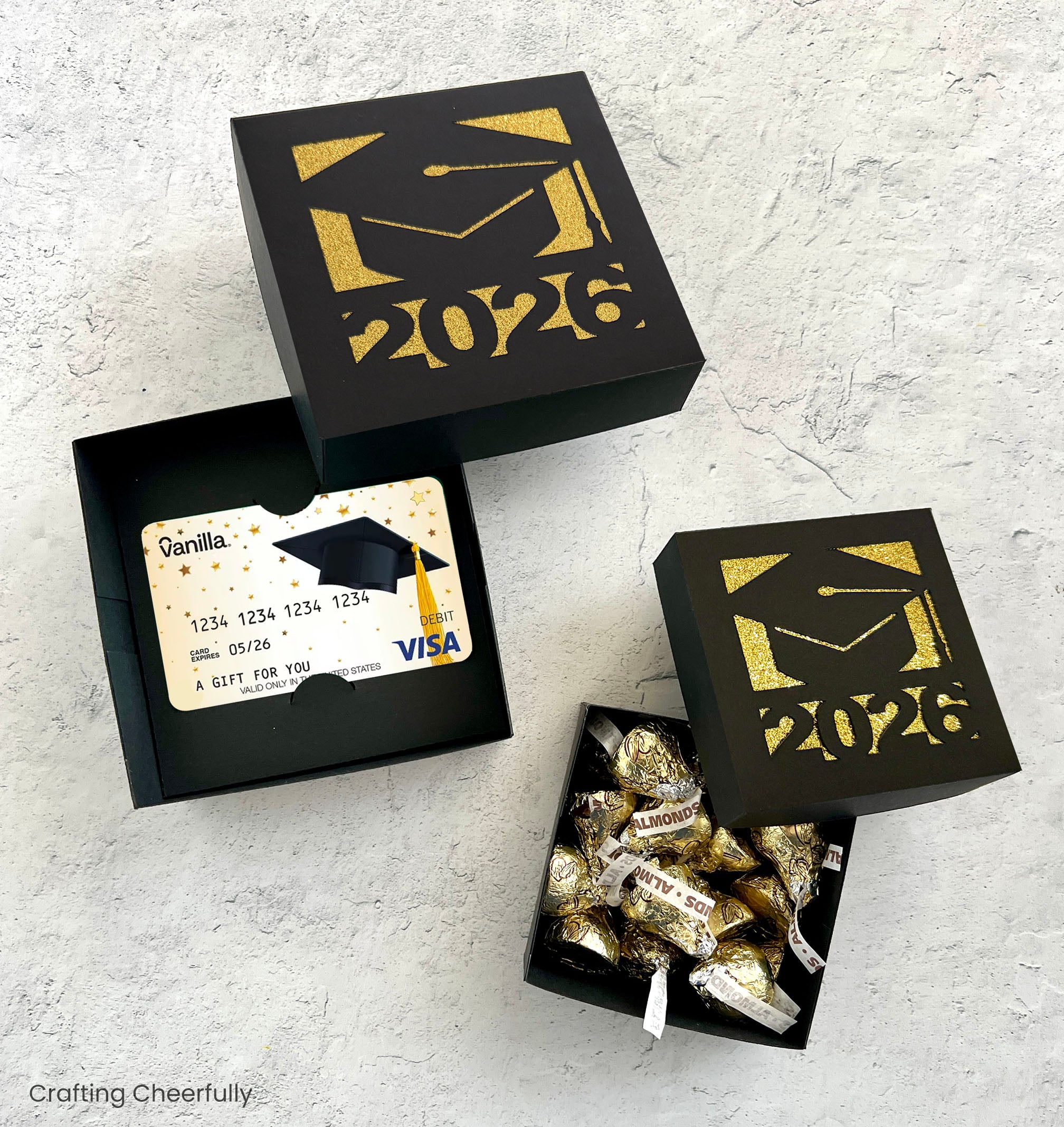 Two square boxes are opened up showing one filled with candy and the other holding a gift card.