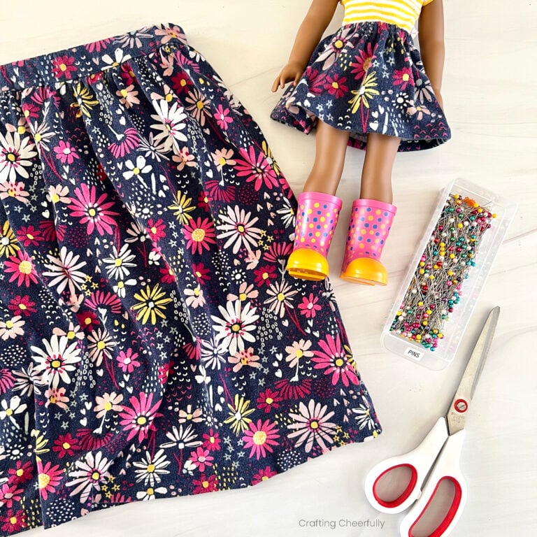 Matching girl and doll skirt lay next to a container of straight pins and a scissors.