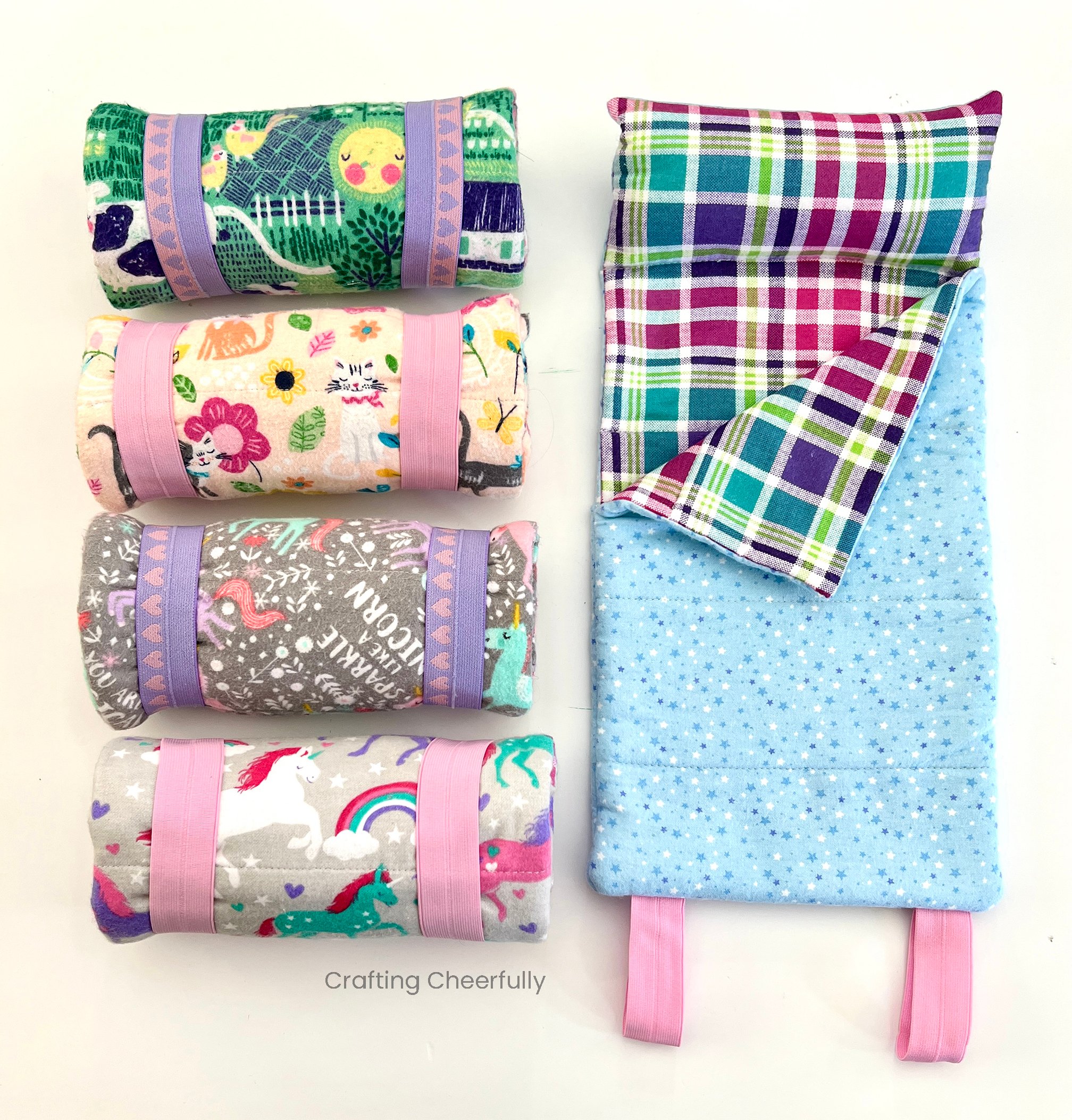 A sleeping bag for dolls is laid open next to four rolled up sleeping bags.
