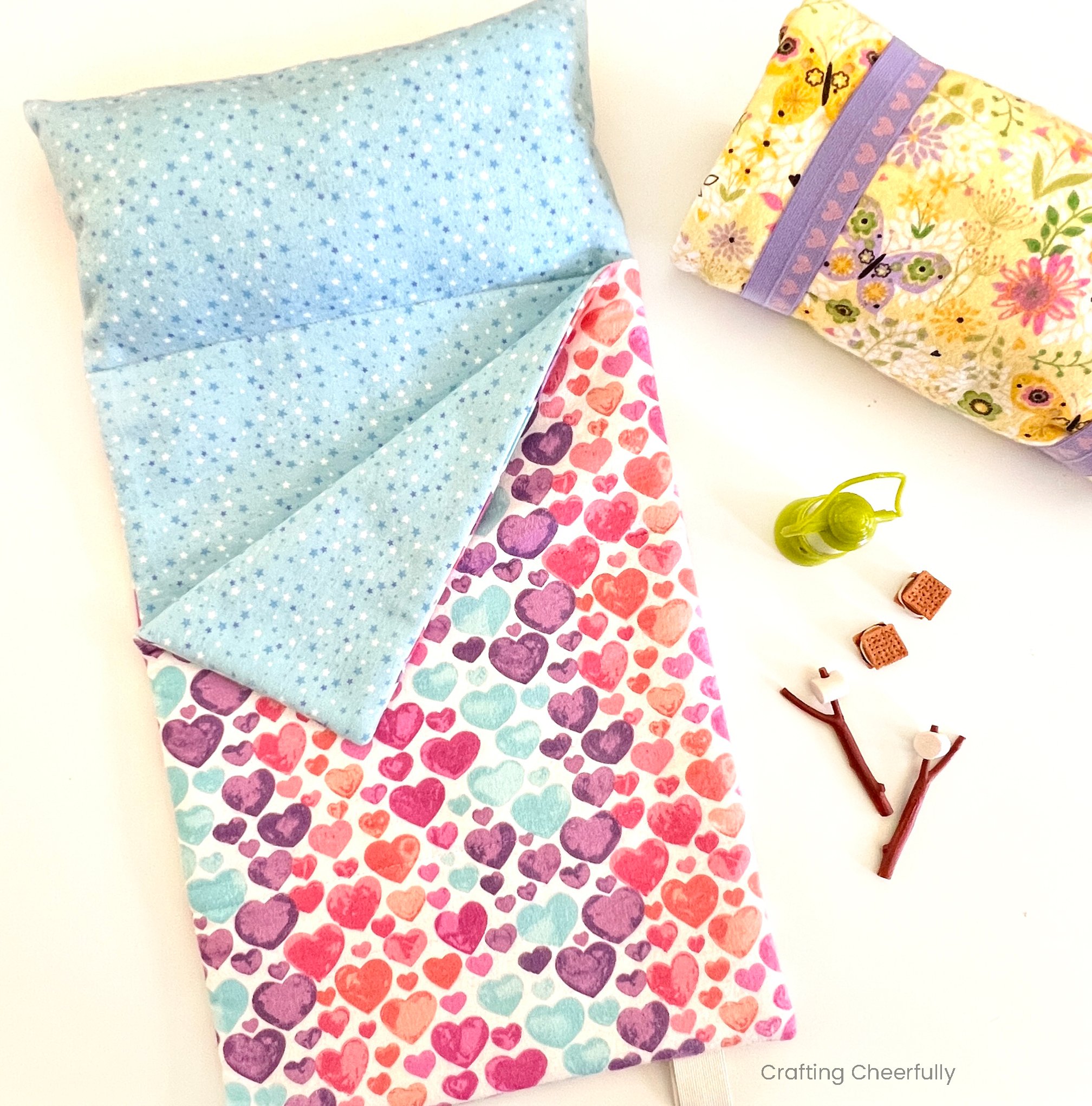Flannel sleeping bag for 18" dolls lays next to a rolled up sleeping bag and cute doll camping accessories.