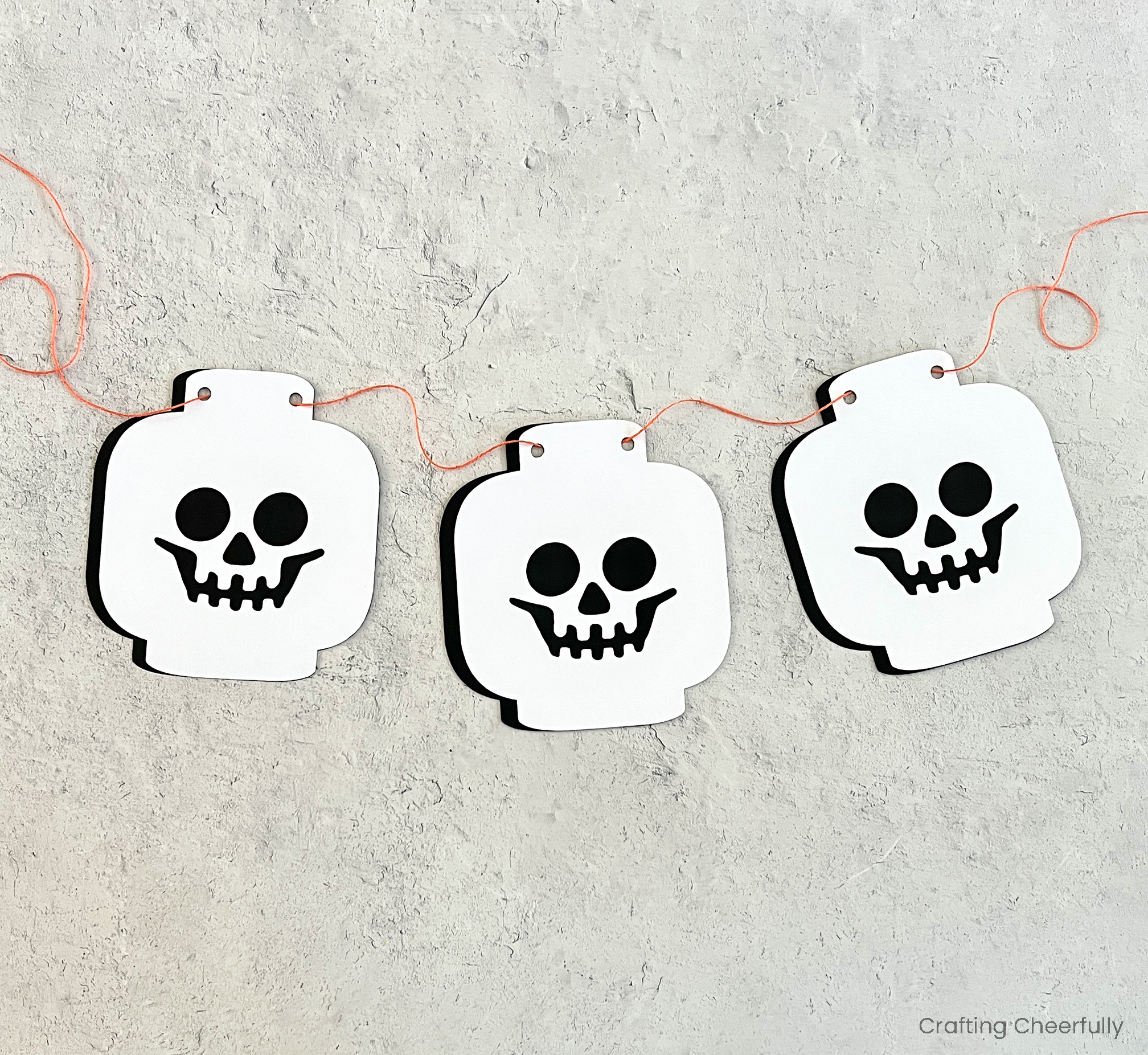 Three paper skeleton heads are strung on a piece of orange twine.