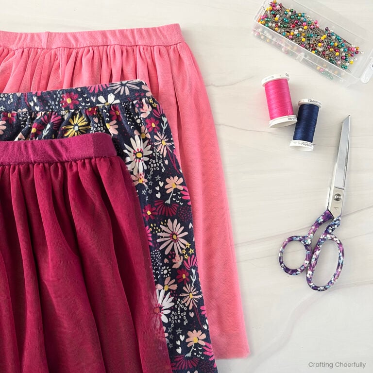 Three girls' skirts lay on a table next to sewing items like pins and thread.