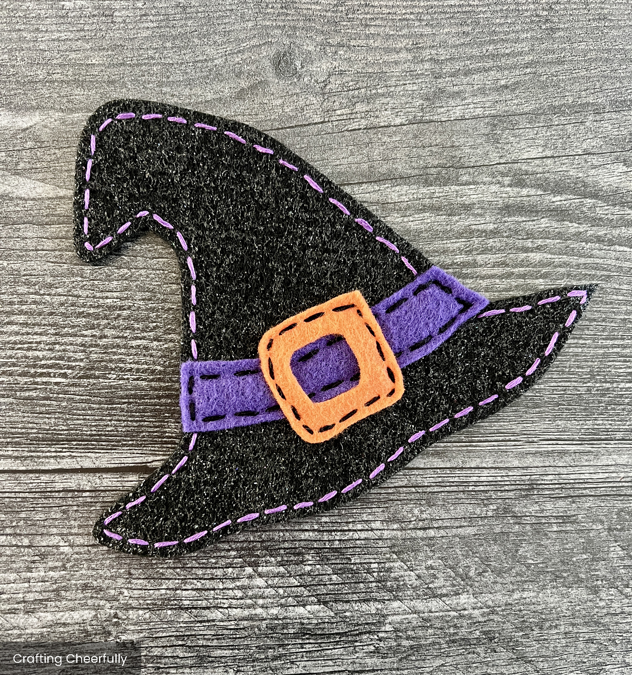 Black felt witch hat is embroidered with orange floss and had a purple buckle.