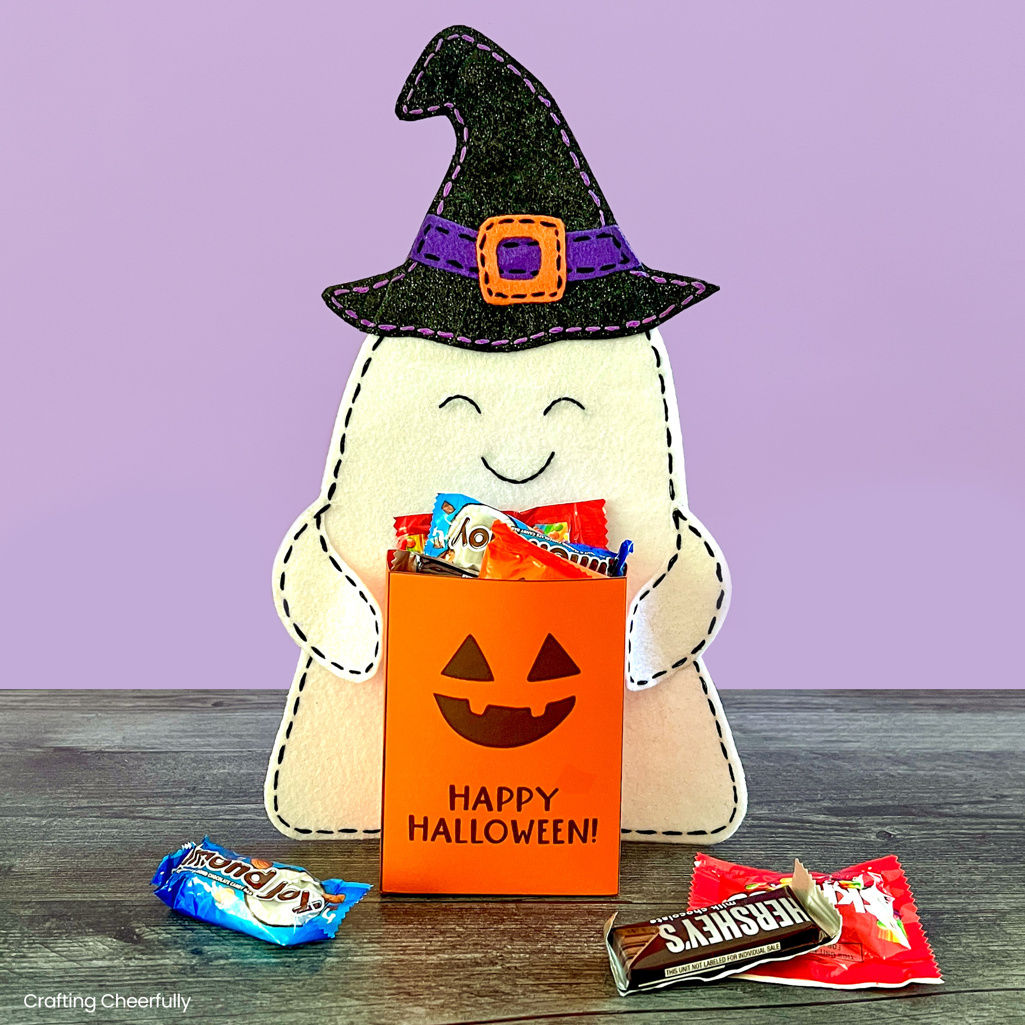Felt ghost holds a pumpkin bag filled with Halloween candy.