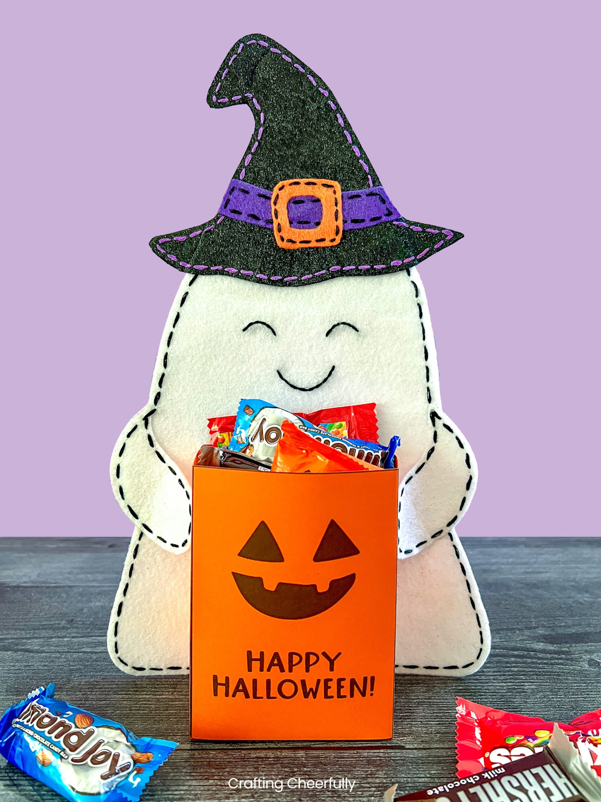 Felt ghost holds a pumpkin bag filled with Halloween candy.