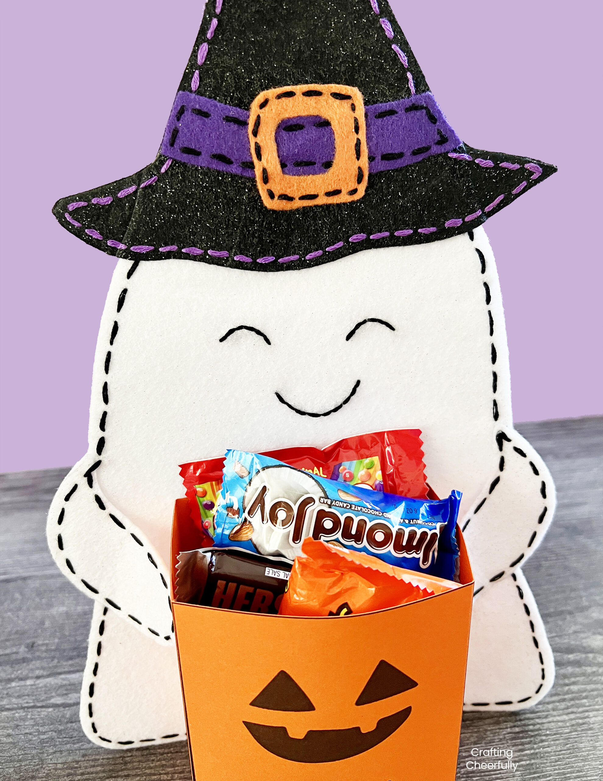 Felt ghost holds a pumpkin bag filled with Halloween candy.