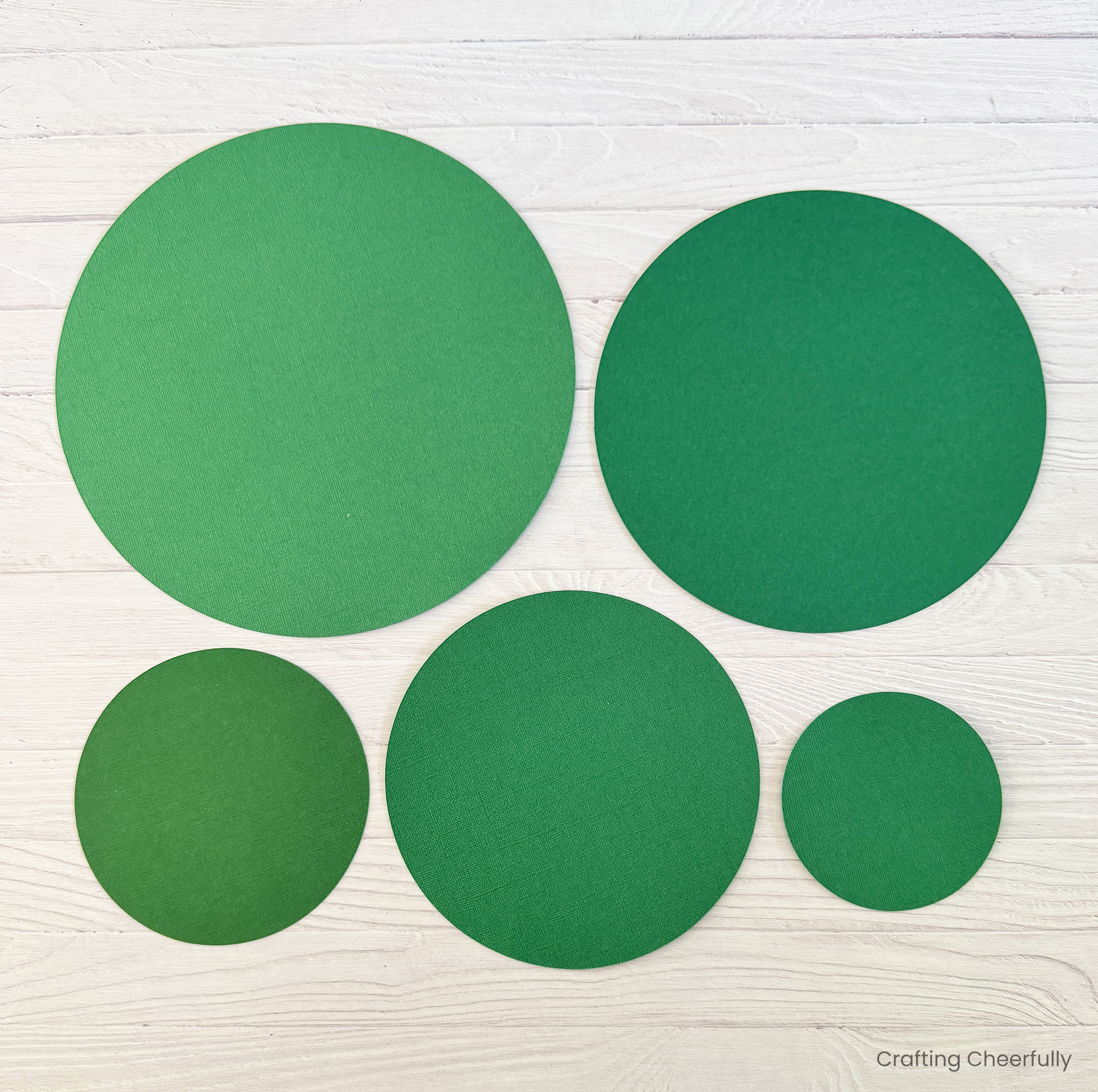 Five round green circles of paper lay on a wood table.