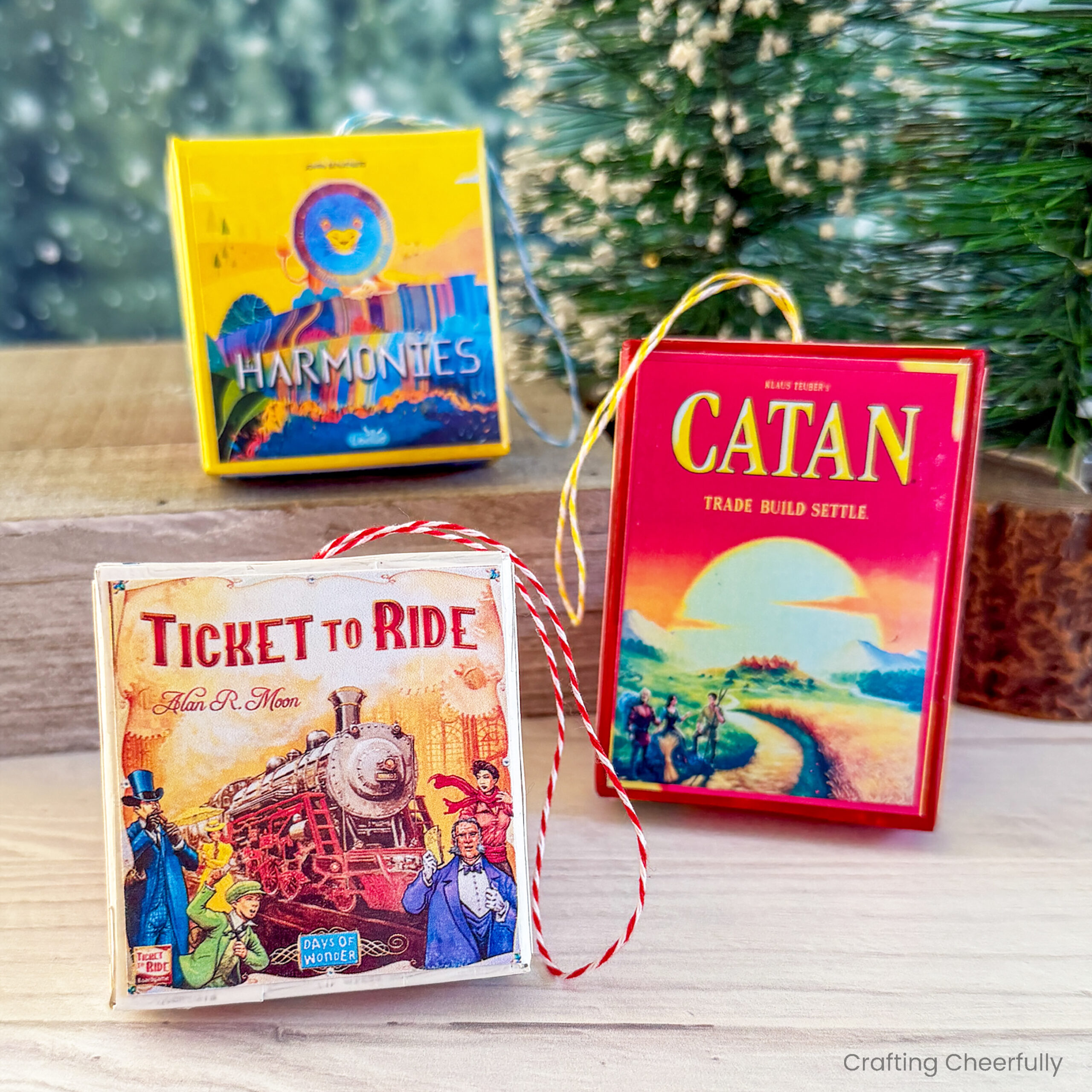 Three handmade board game ornaments are placed on a wood table near a bottlebrush tree.