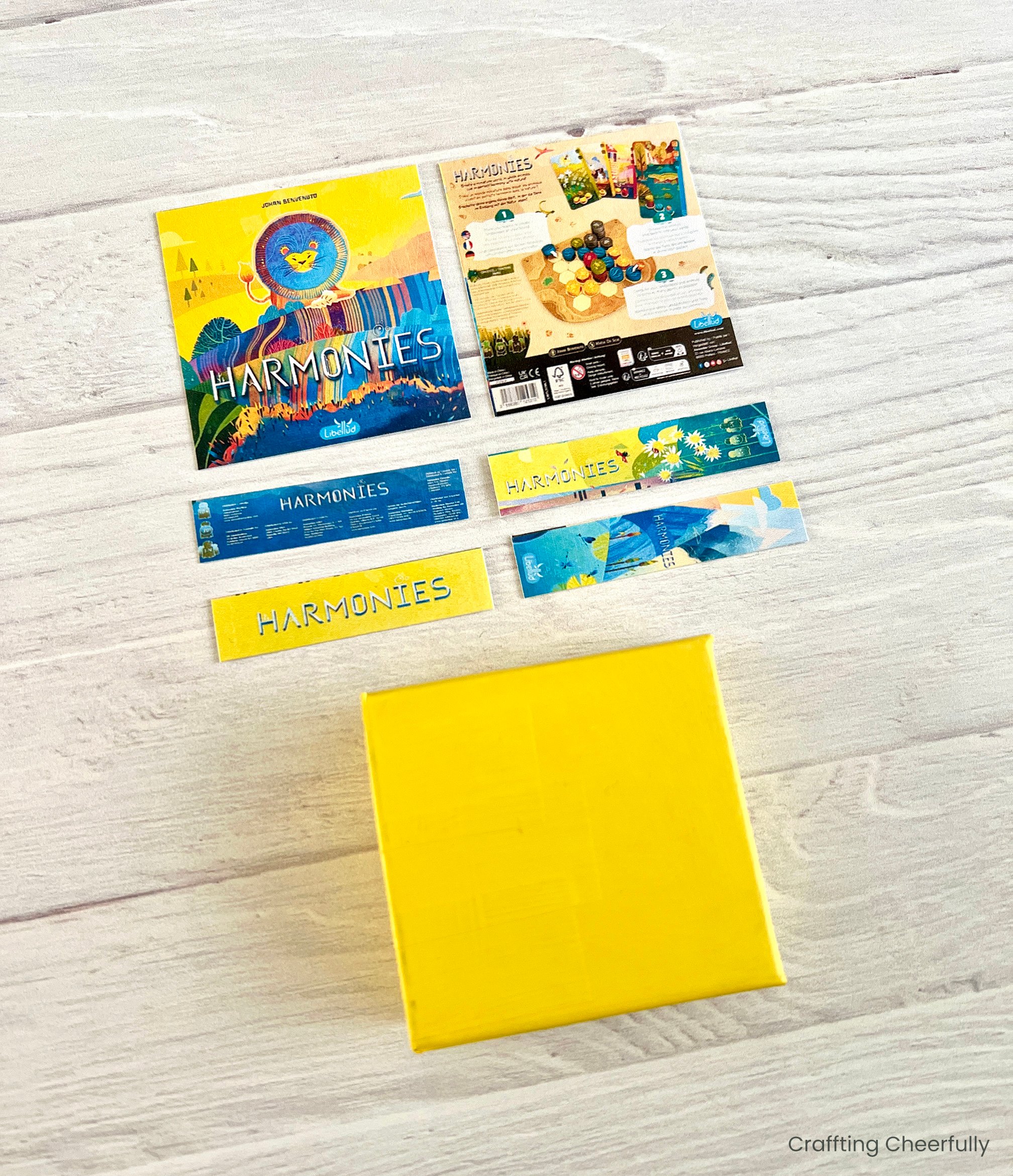 The graphics for all six sides of the board game ornament are laying next to a the yellow-painted box.