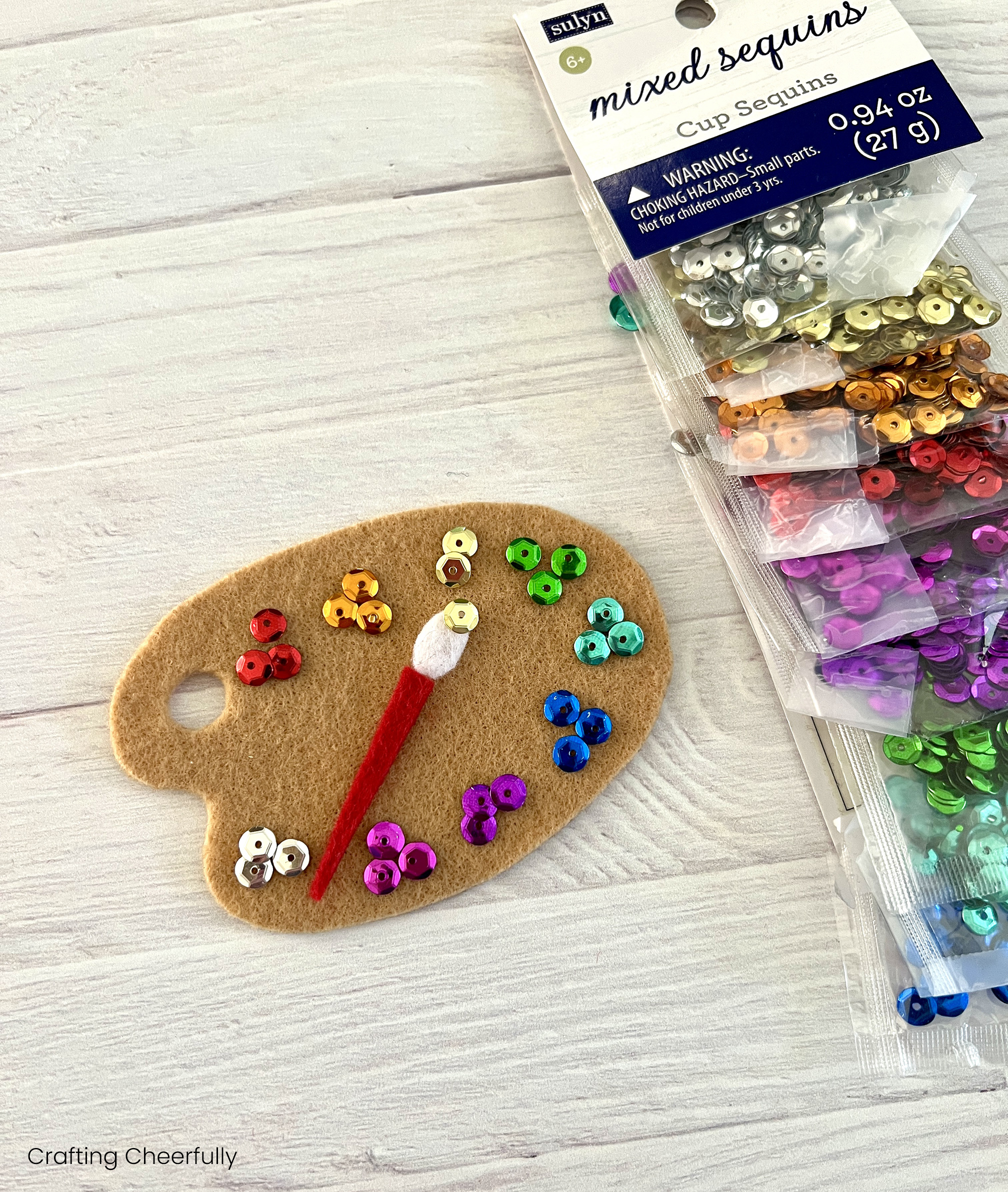 Sequins and a felt paint brush are arranged on the tan palette.