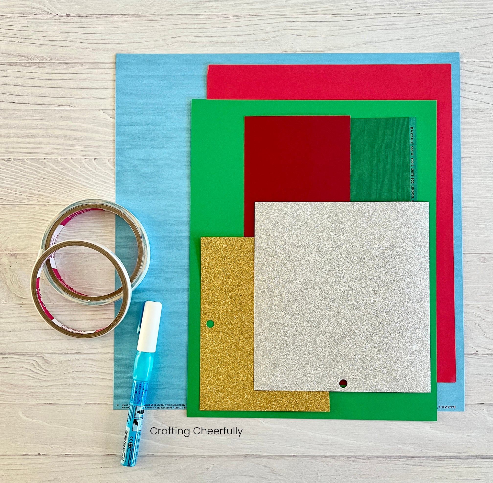 Supplies needed for mailbox card including cardstock in reds, greens, gold, silver and light blue along with adhesive.