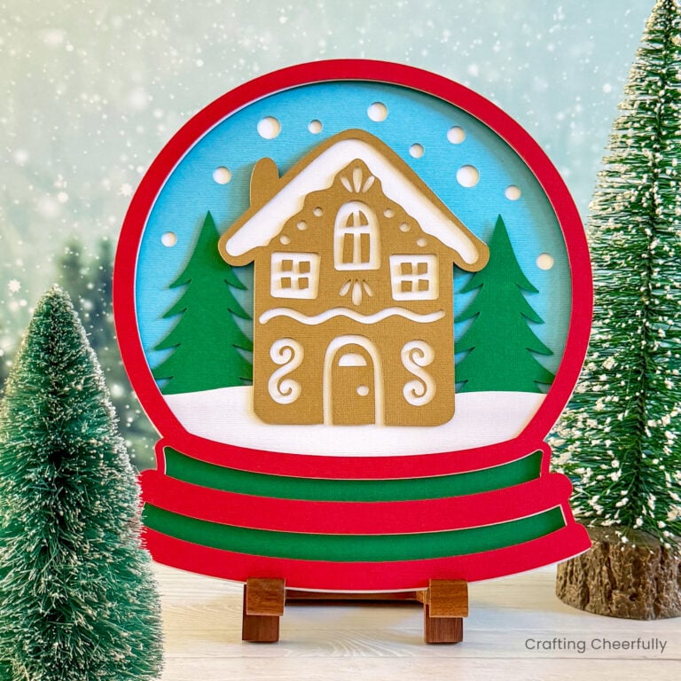 Layered paper snow globe with gingerbread house made from paper.