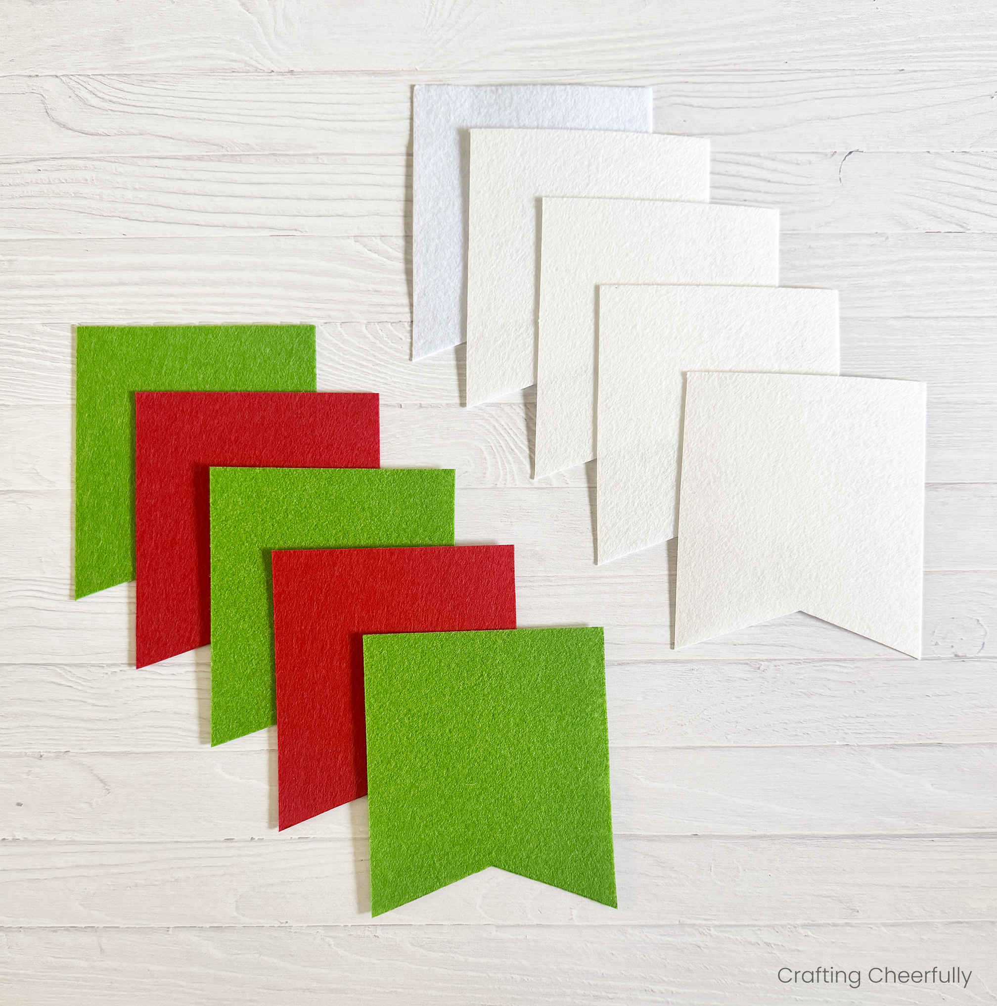 Five white felt pennants and 5 red and green felt pennants lay on a table.