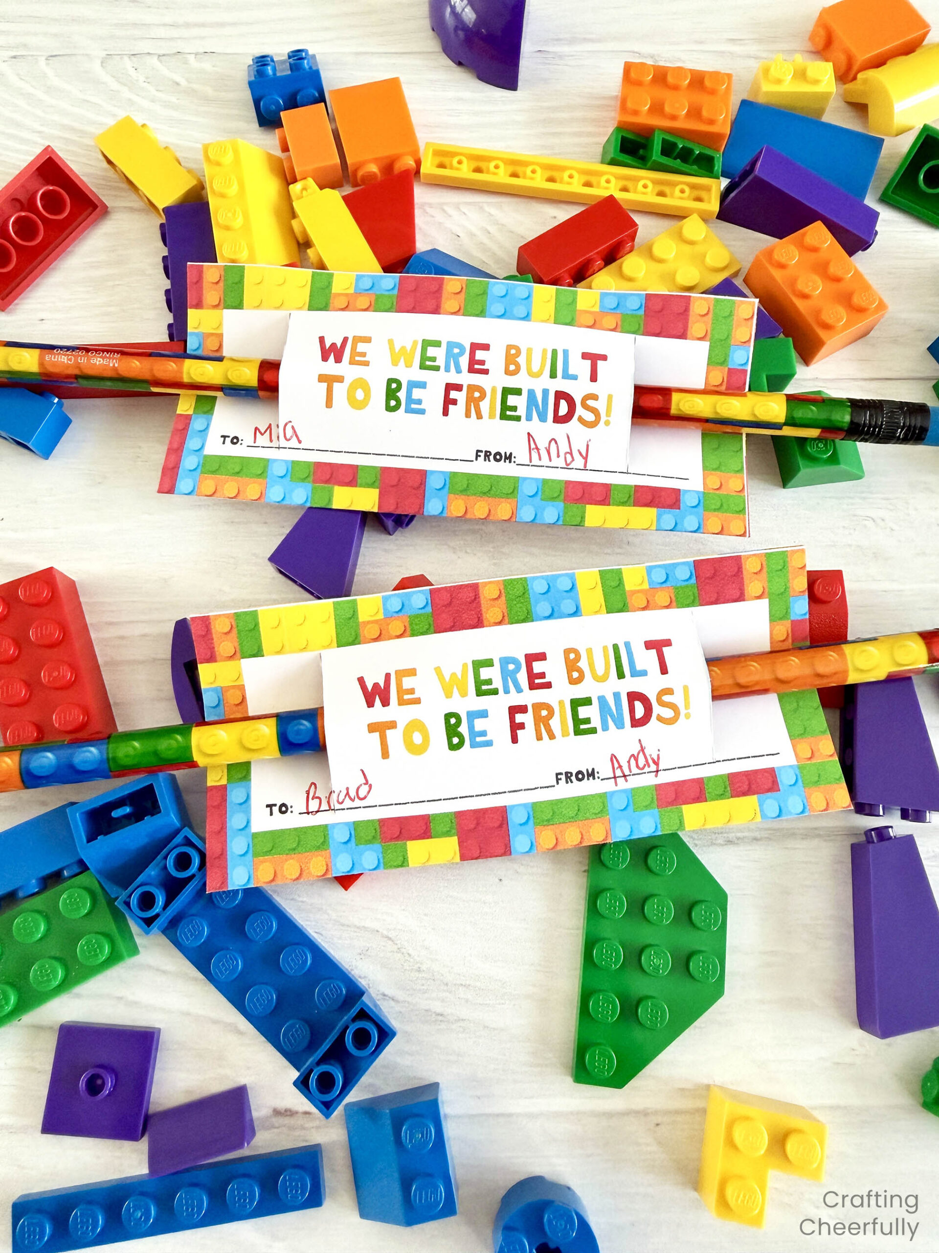 Two lego-themed valentines on pencils lay on top of a pile of colorful Lego bricks.