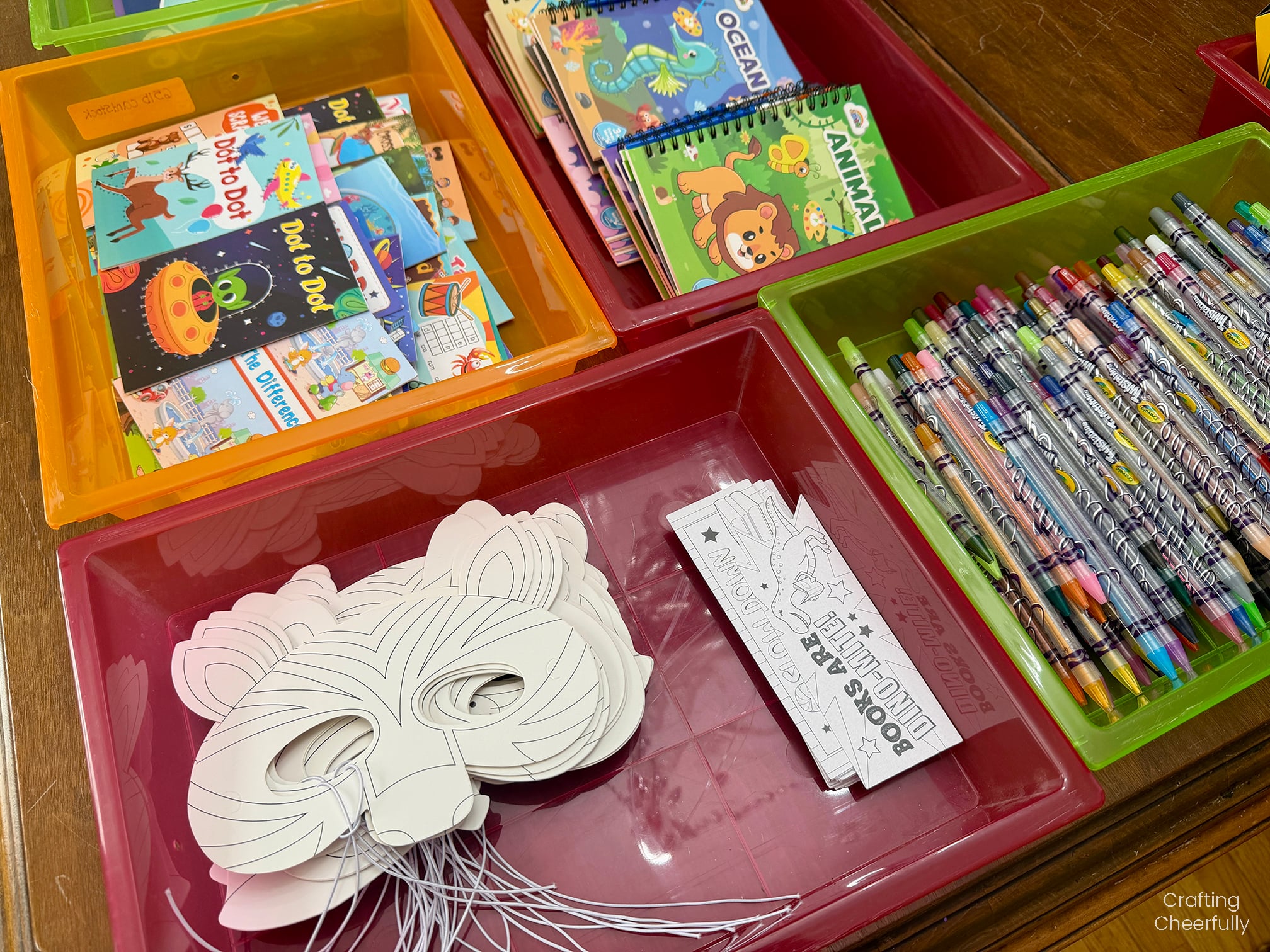 Coloring page masks, bookmarks, twistable colored pencils and more lay in trays on a table.