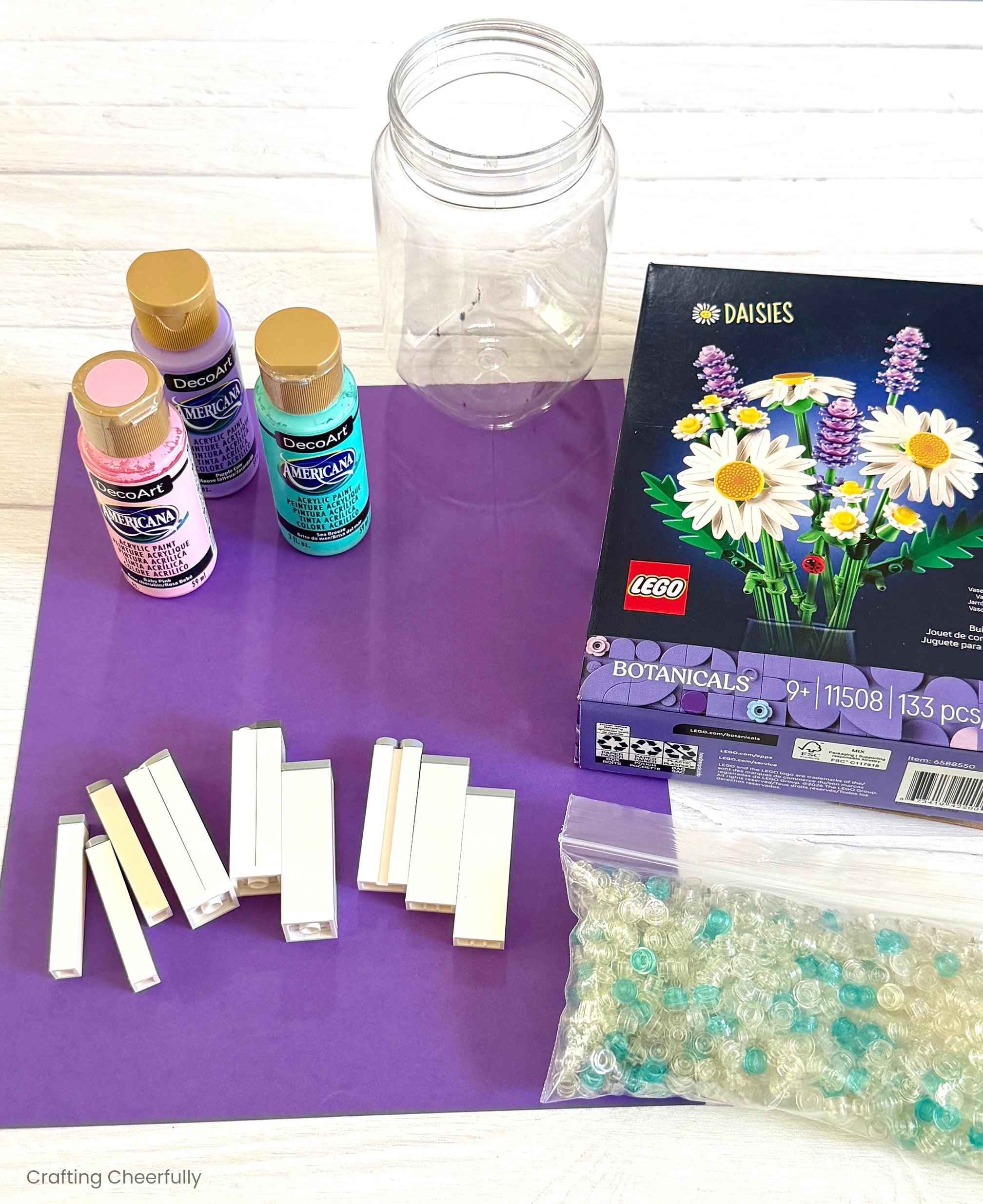 Purple paper, LEGO stamps, paint, mason jar, bag of LEGO pieces and a boxed LEGO set of botanical daisies.