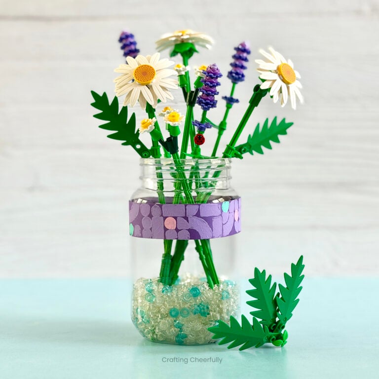 Mason jar filled with LEGO botanicals is decorated with a strip of purple paper that is stamped with LEGO pieces.