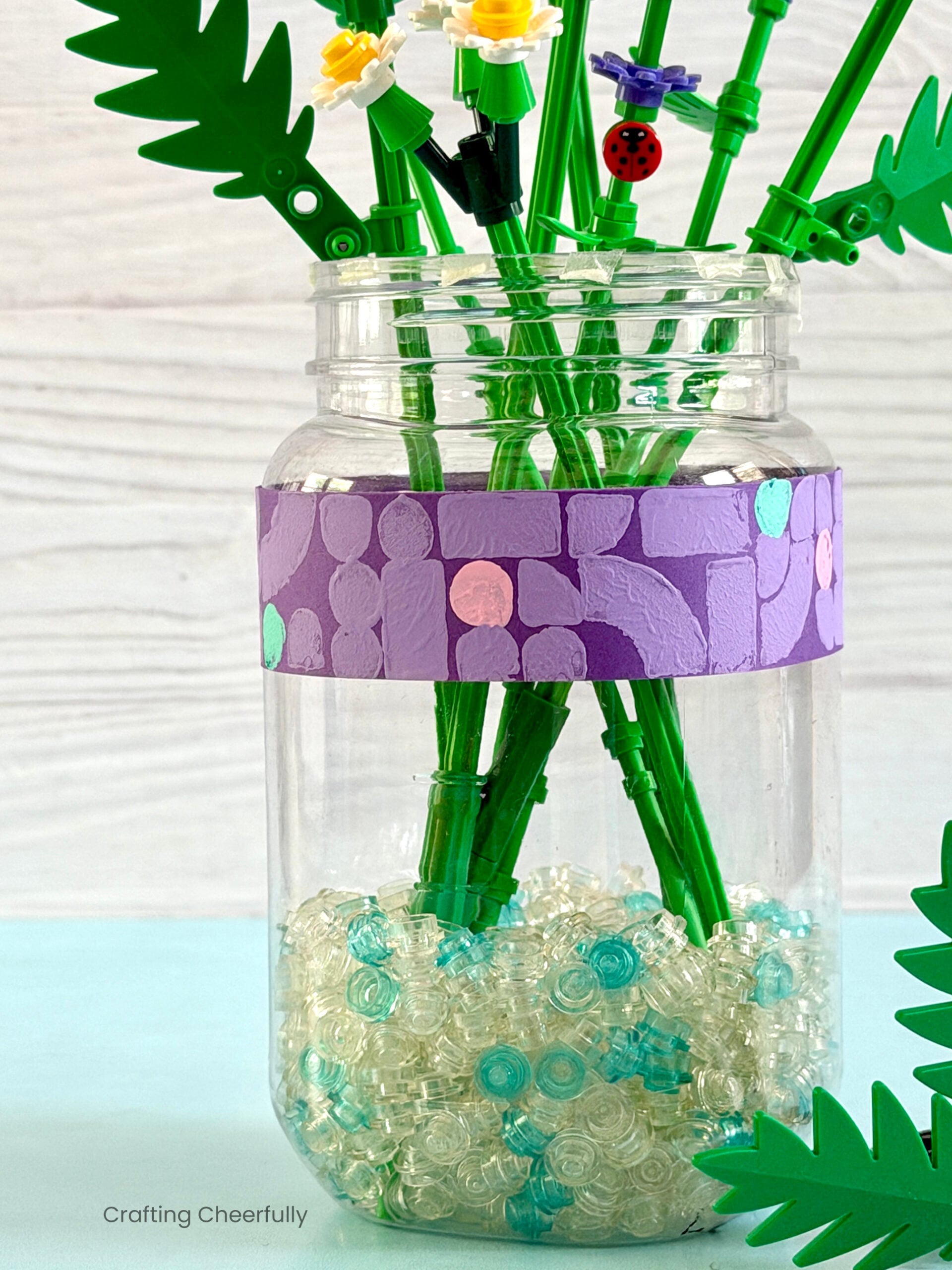 Mason jar filled with LEGO botanicals is decorated with a strip of purple paper that is stamped with LEGO pieces.