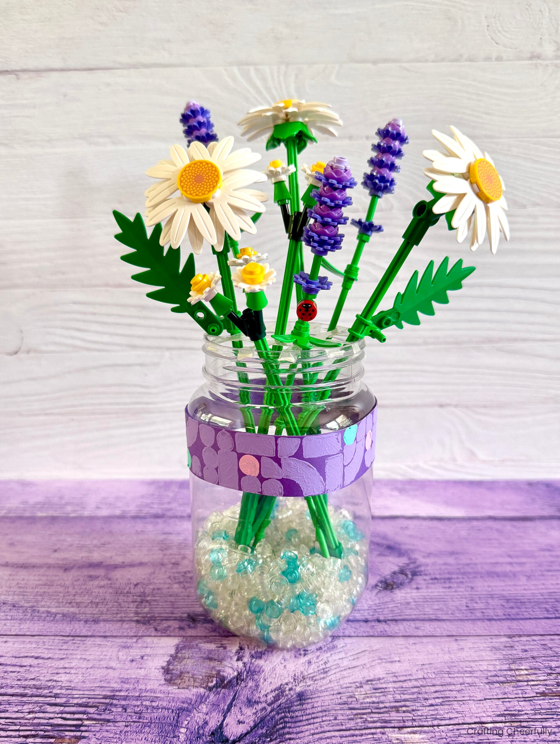 Mason jar filled with LEGO botanicals is decorated with a strip of purple paper that is stamped with LEGO pieces.