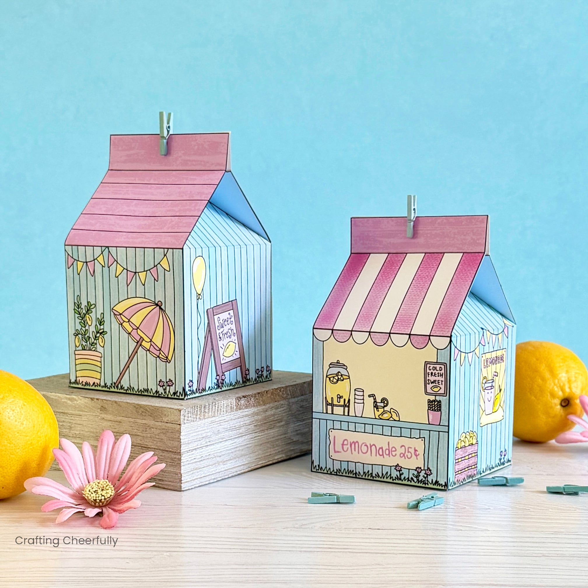 Two Lemonade stand treat boxes sit next to lemons and pink flowers.