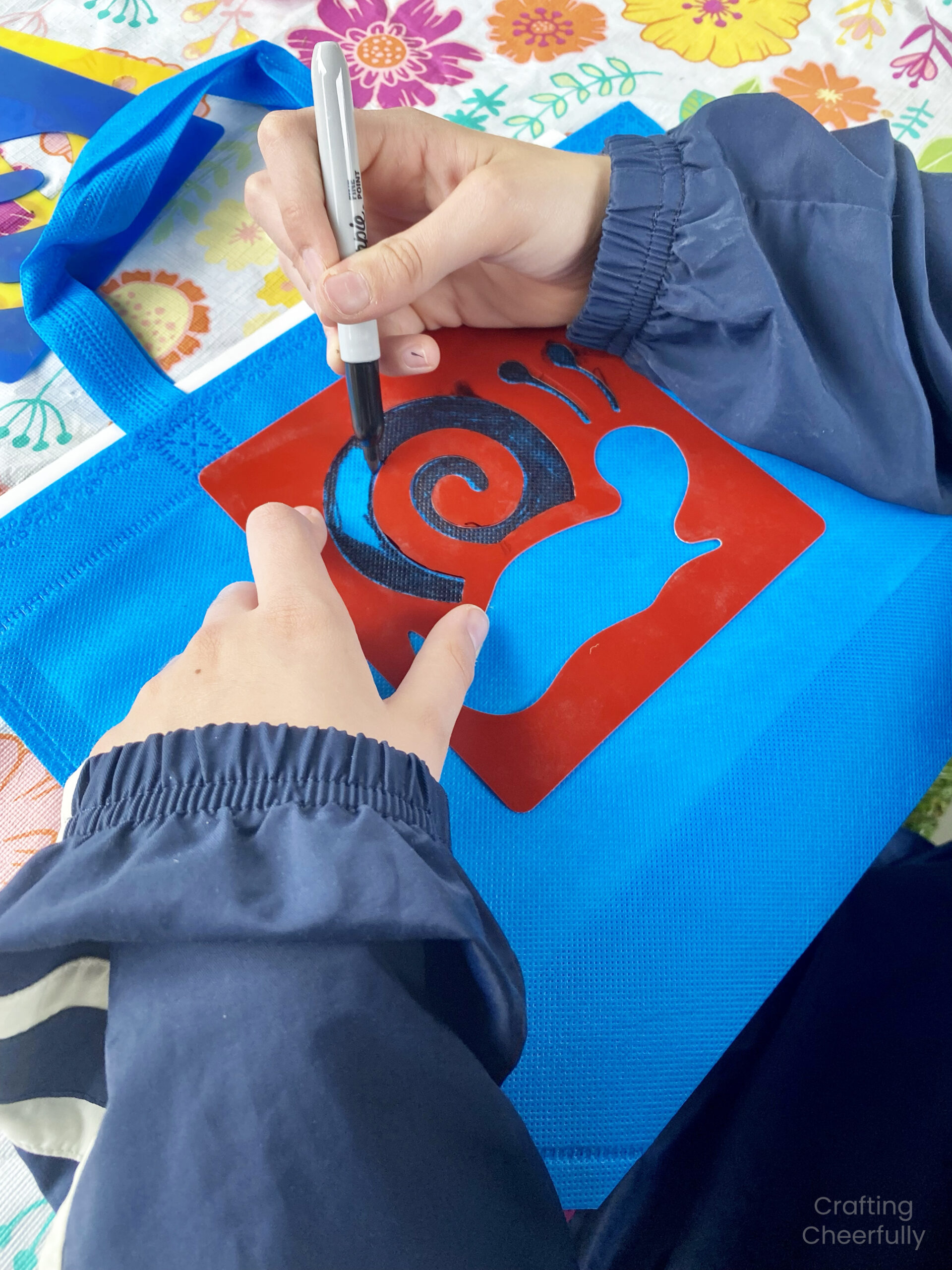 A child uses a stencil to add a snail design to the front of a resusable bag.