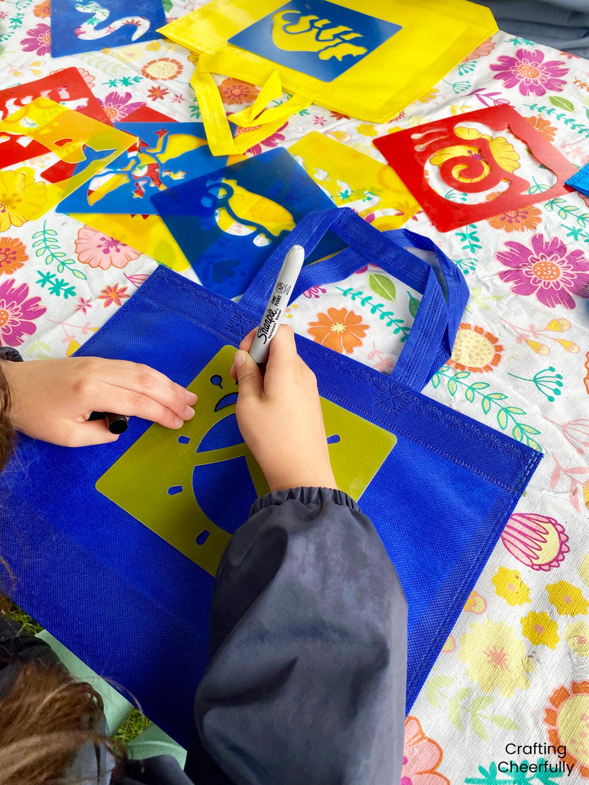 A child uses a stencil to add a ladybug design to the front of a resusable bag.
