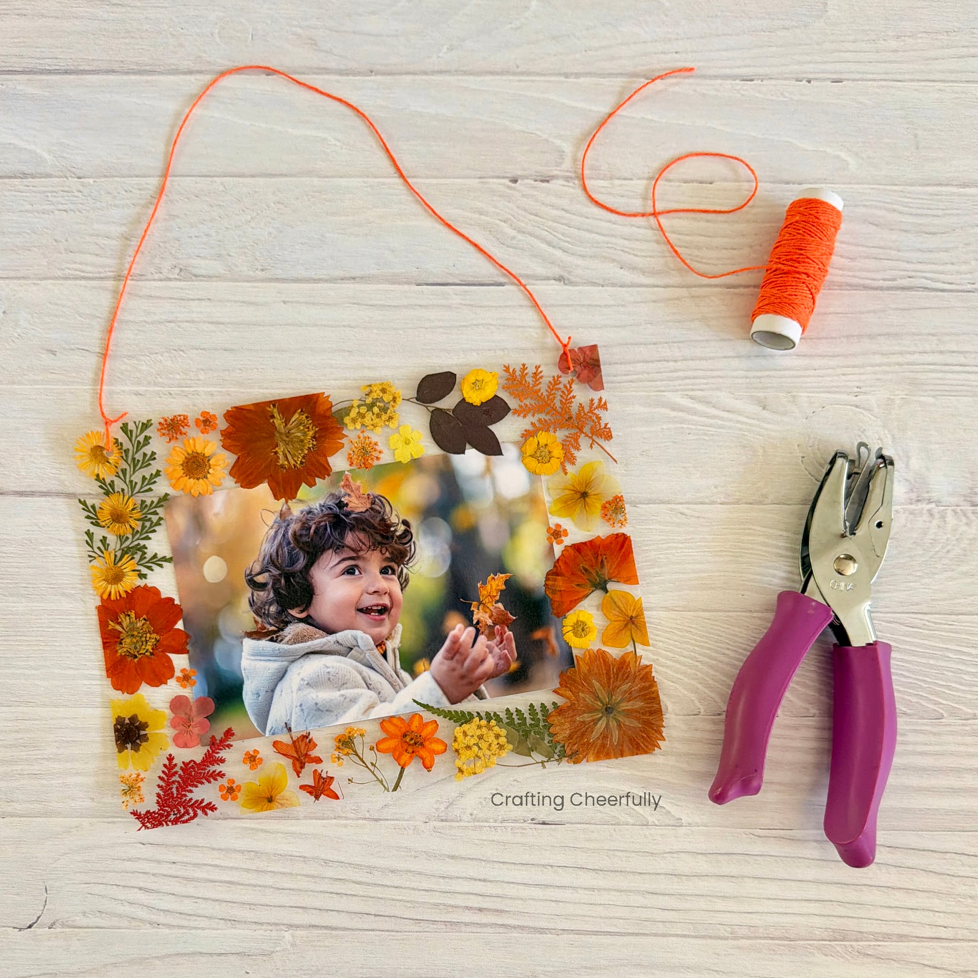 A hole punch and roll of Baker's Twine lays next to the autumn leaf frame.