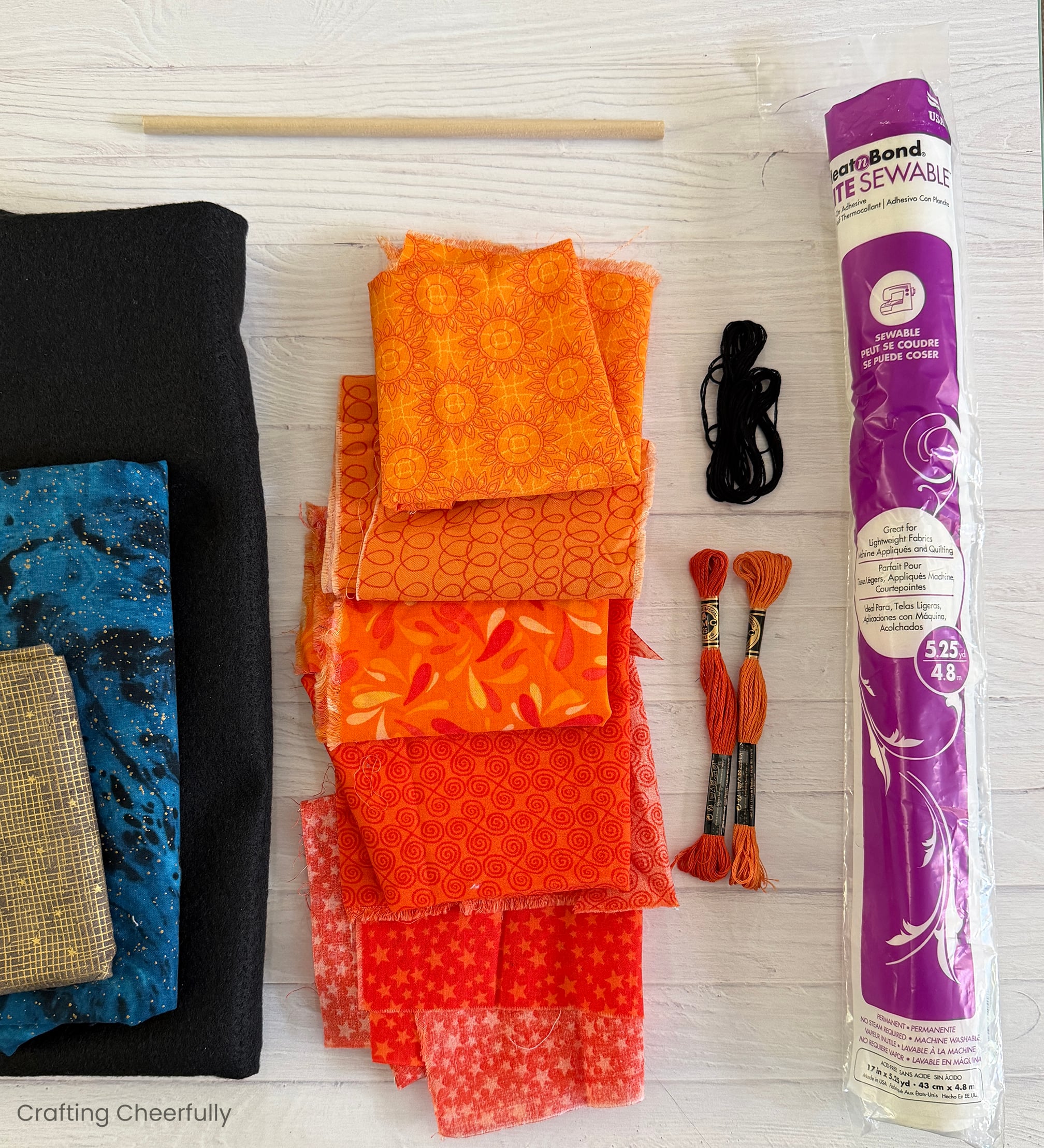 Supplies like fabric, felt, embroidery floss, and fusible interfacing lay on a white wood table.