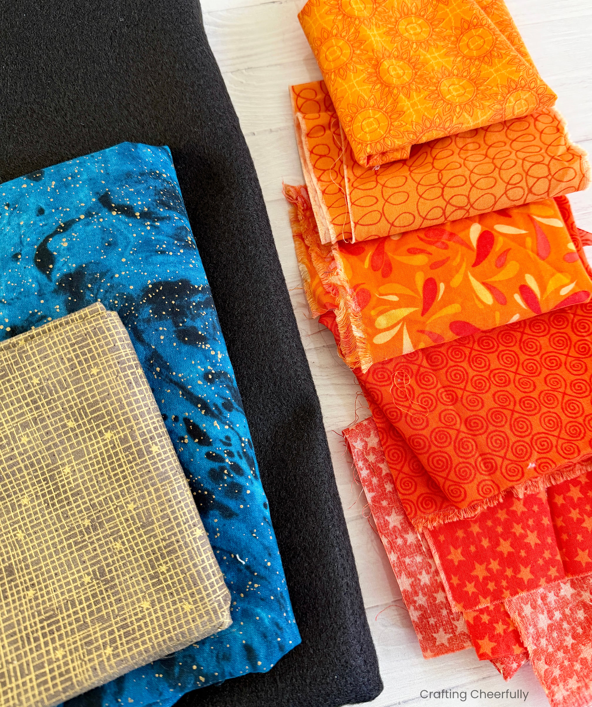 Fabric scraps in different shades and patterns of orange lay next to black felt and blue fabric.