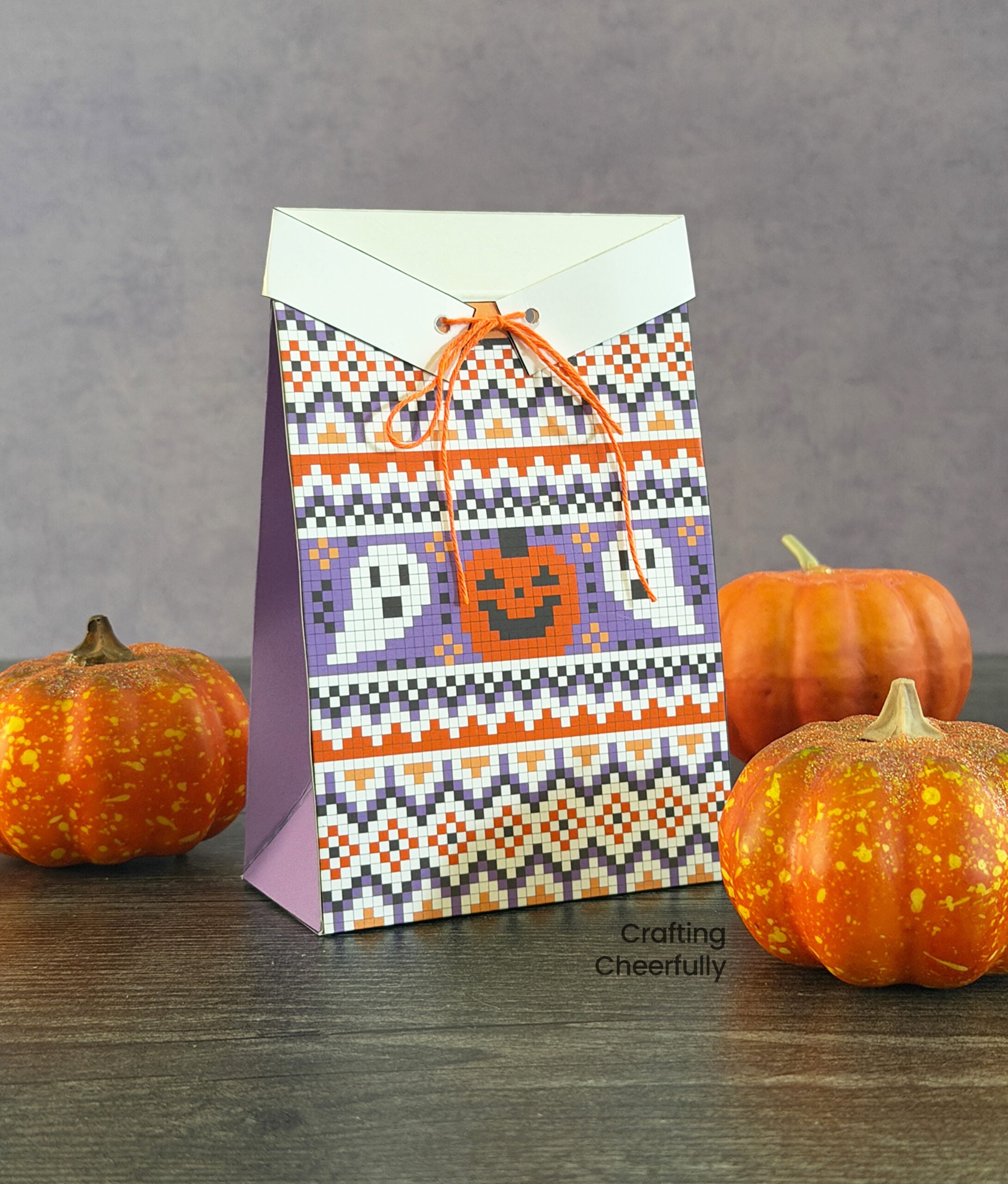 A treat box is designed to look like a purple, orange and white sweater with a jack-o’-lantern and two ghosts on the front of it.