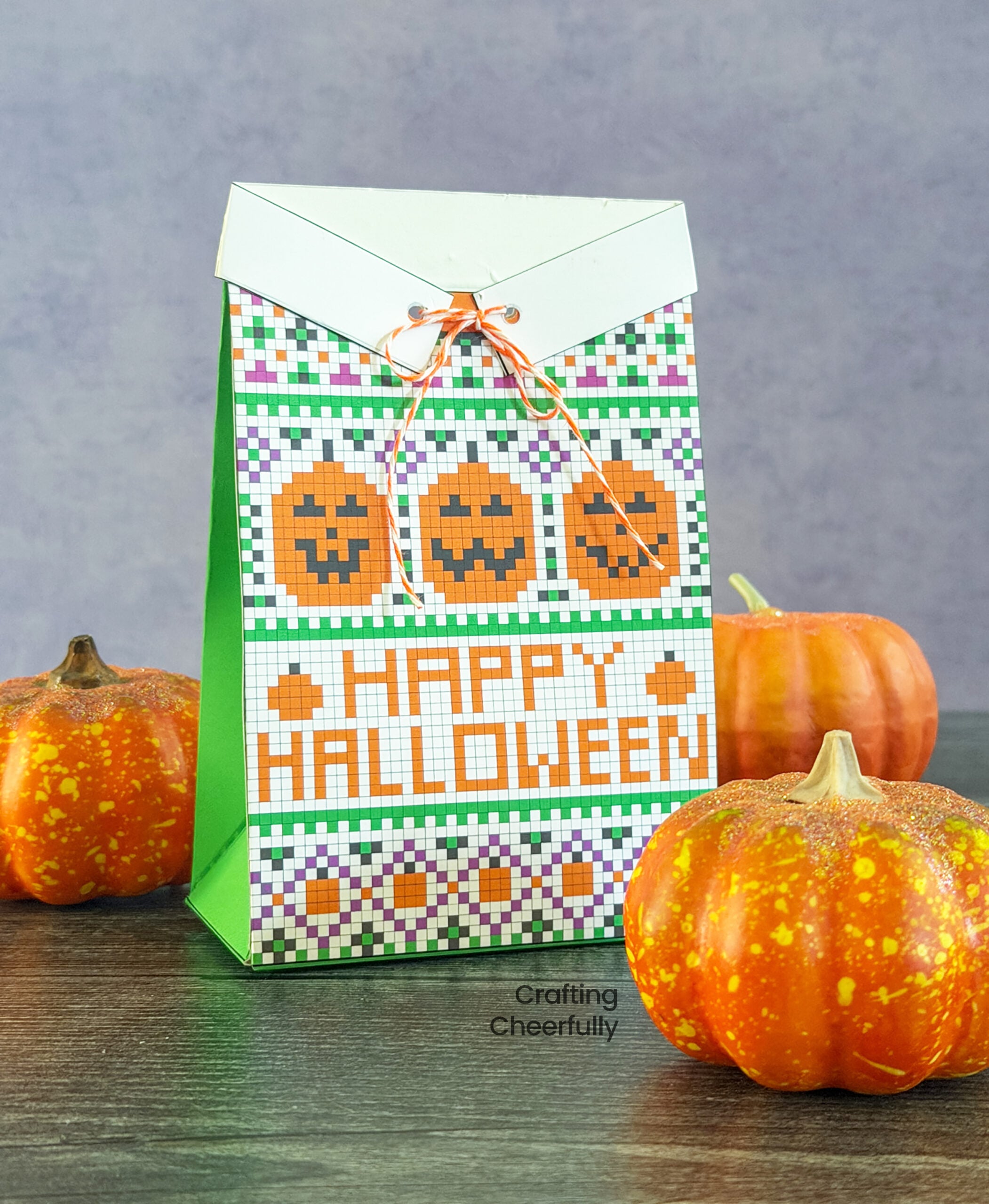 A treat box is designed to look like a colorful Halloween sweater with three smiling jack-o’-lanterns and the words “Happy Halloween” on the front of it.